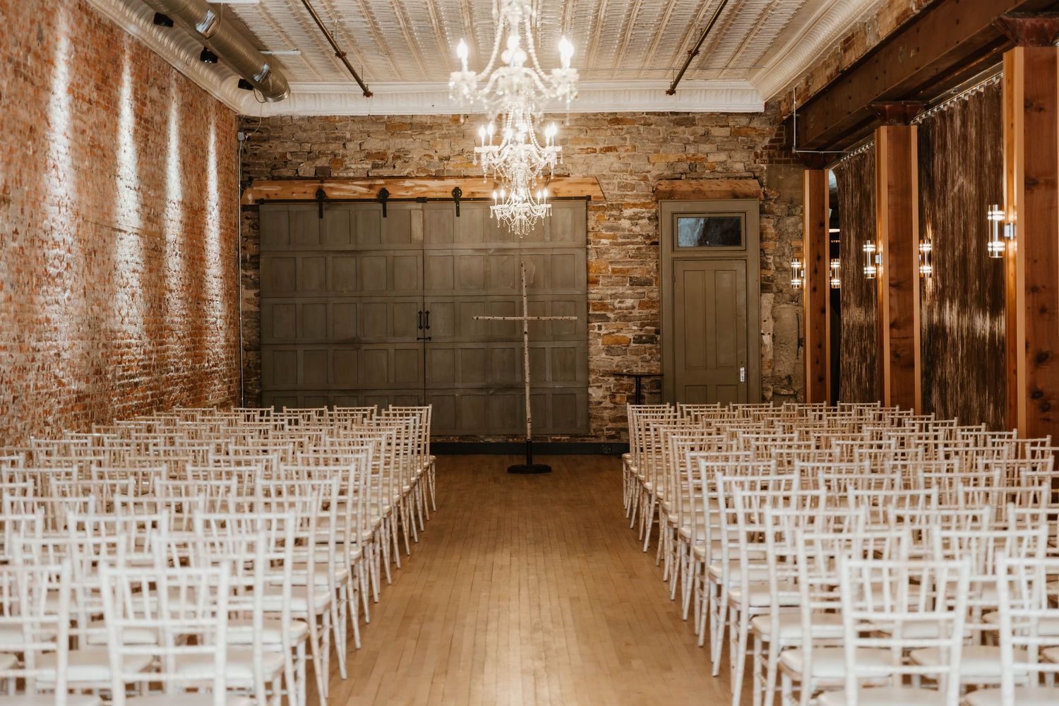 Wedding ceremony venue with white chairs and exposed brick walls illuminated by crystal chandeliers.