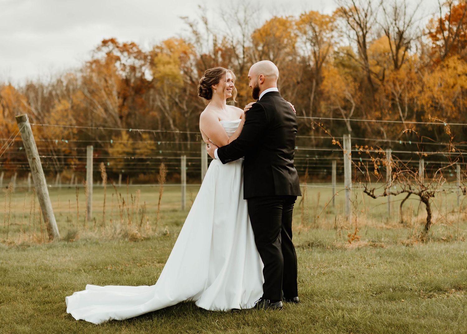 Autumn wedding scene in field with golden trees in background.