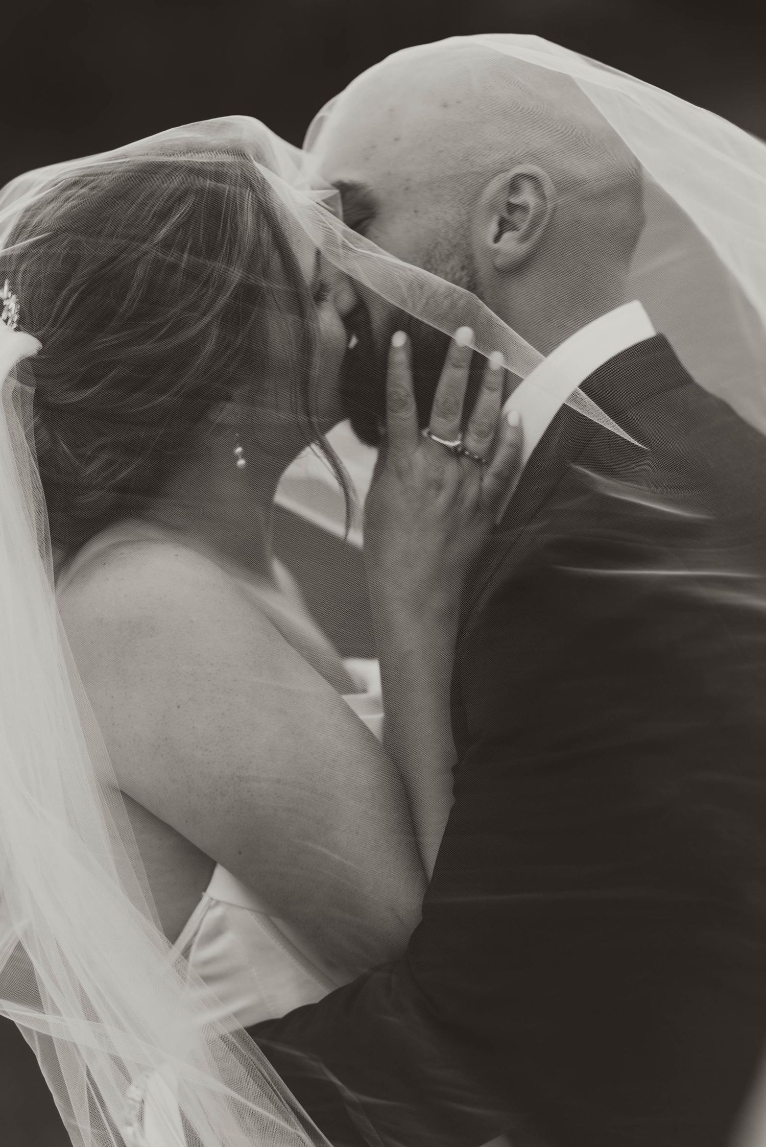 Intimate black and white portrait of wedding couple sharing tender moment under veil.