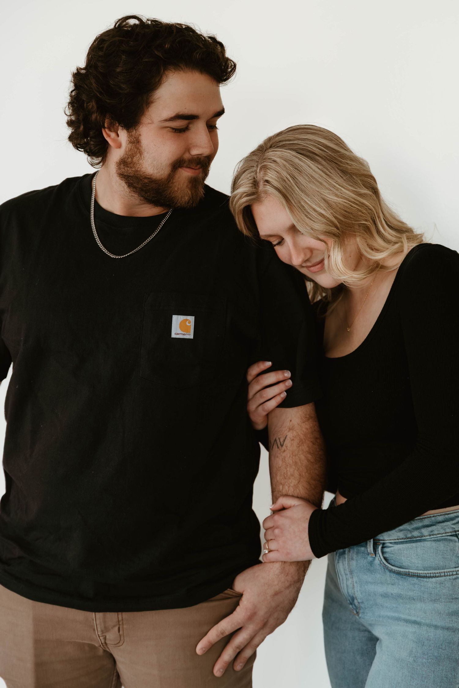 A couple in black sweaters share an intimate moment against a white background.