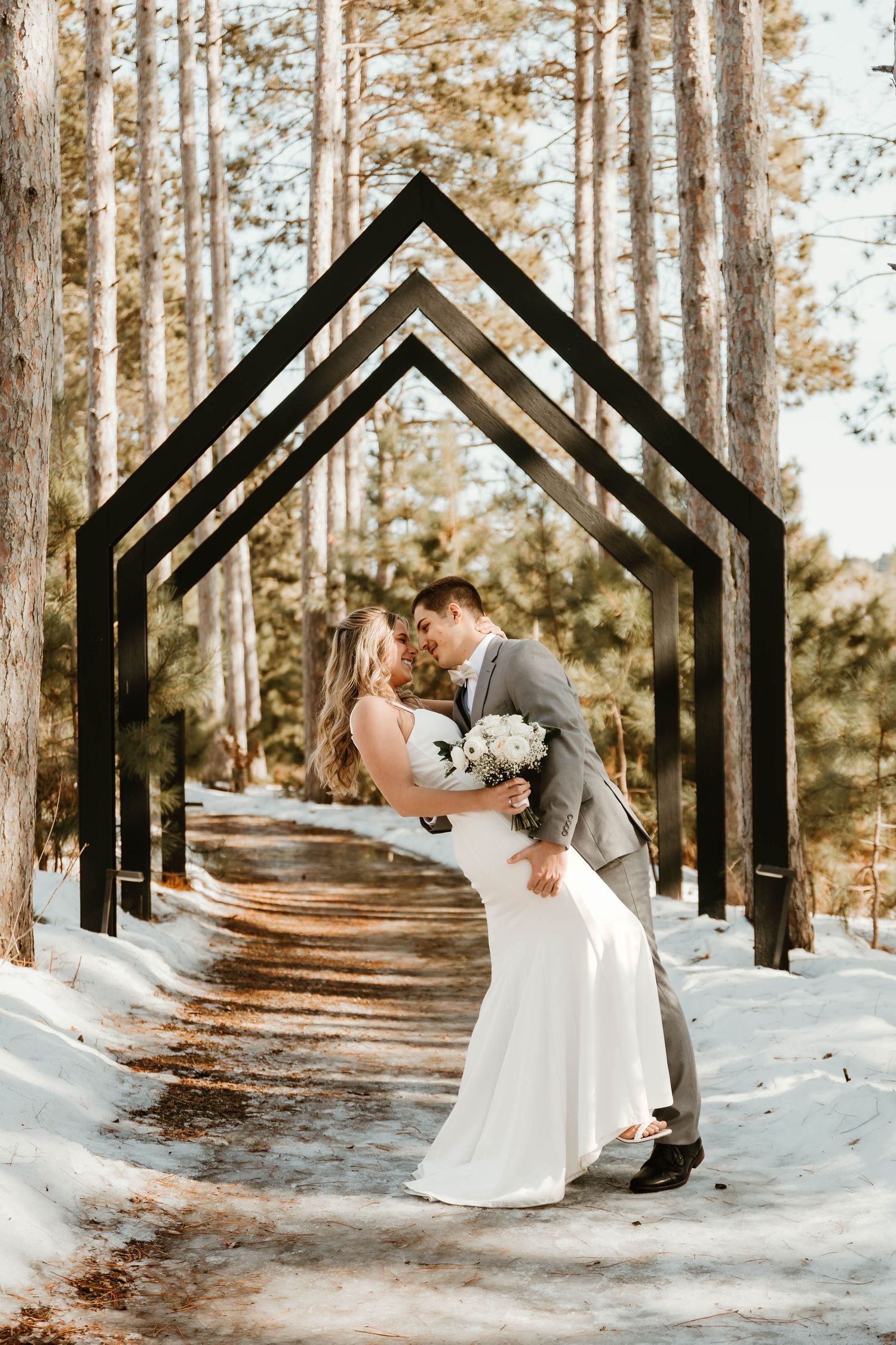 Couple sharing intimate moment under black geometric arches in snowy forest setting.