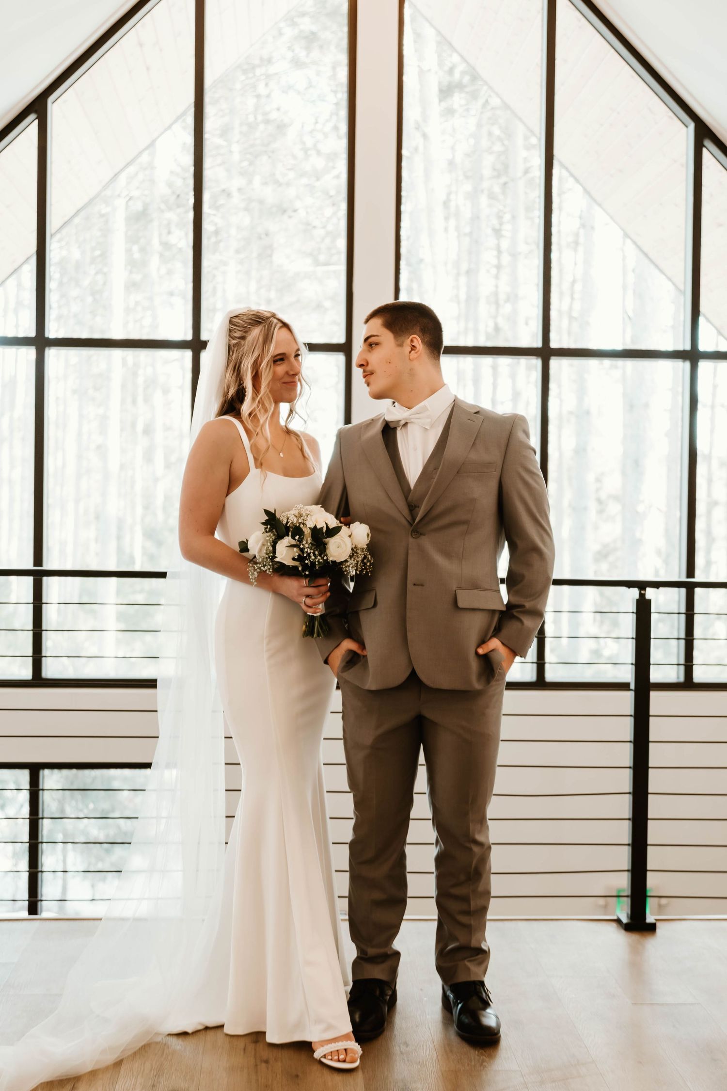 A couple poses for their wedding photos in a modern venue with large windows.