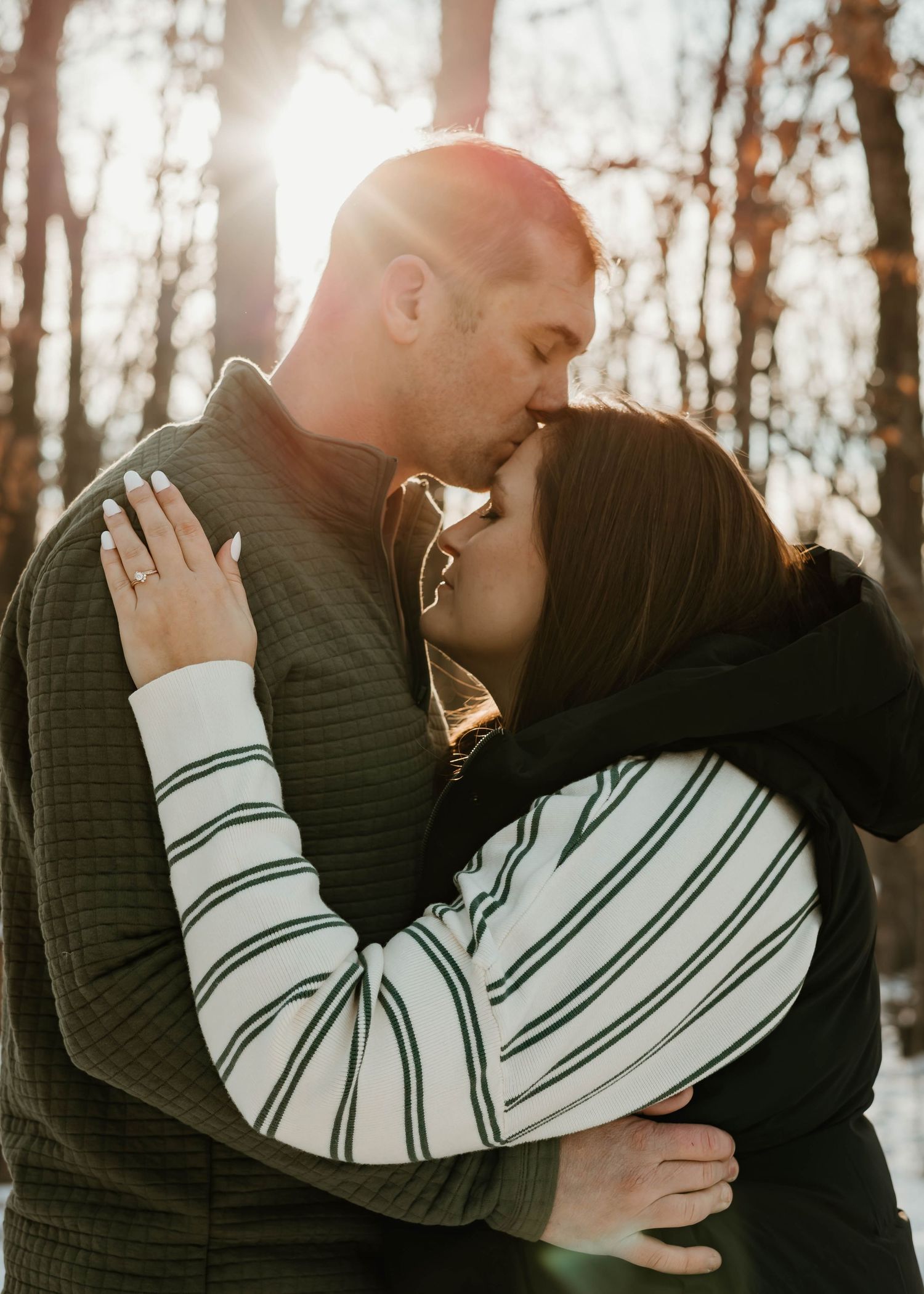 A romantic couple embraces in a sunlit forest during golden hour.