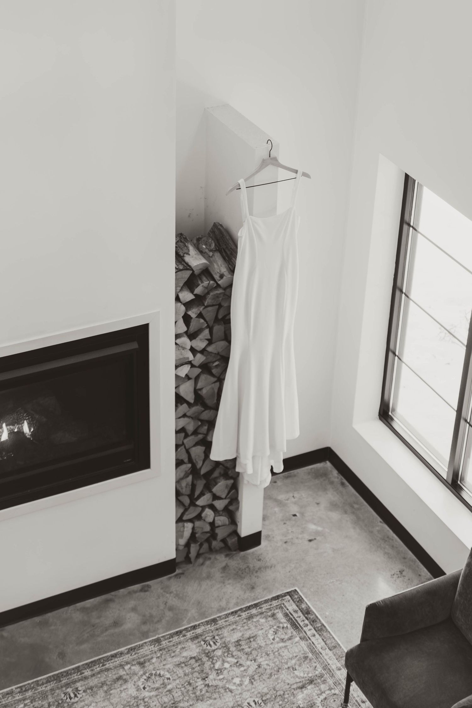 White wedding dress hanging by fireplace with stacked firewood and modern decor.