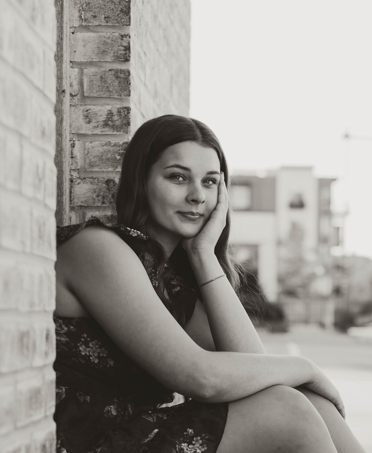 Black and white portrait of a young woman leaning against a brick wall, resting her chin on her hand.