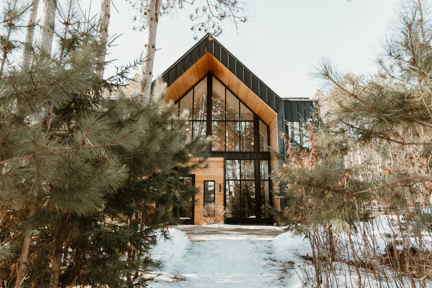 A cozy A-frame cabin nestled in a snowy forest setting with large windows and natural wood exterior.