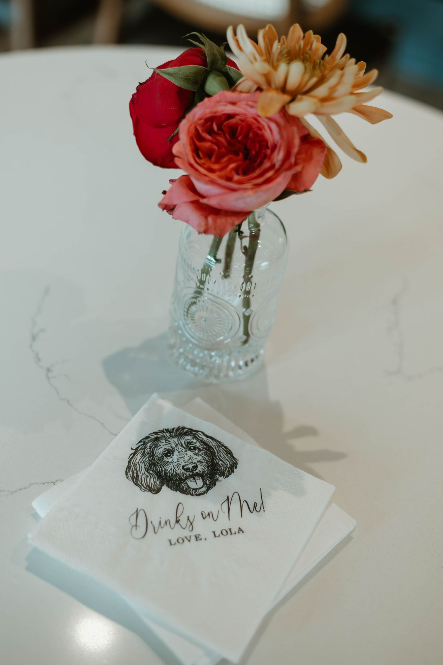 Small floral centerpiece with red and peach roses in a crystal vase next to wedding stationery.