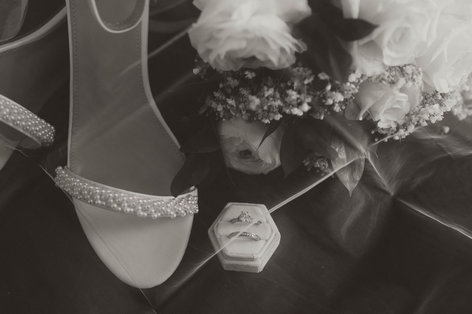 A wedding dress hangs elegantly against a dark background with delicate lace and tulle details.