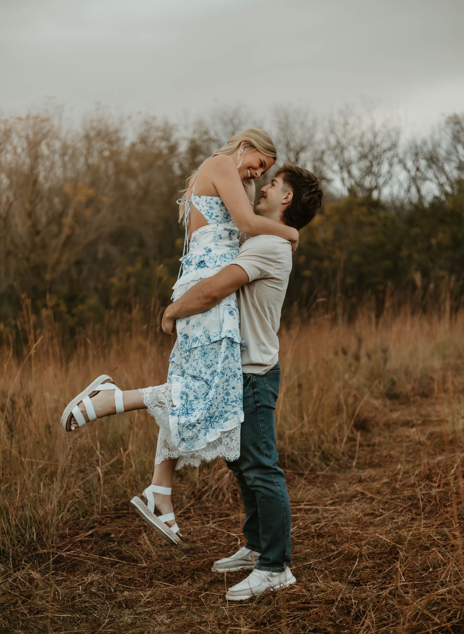 Two figures embrace in a romantic dance pose against a backdrop of autumn fields and bare trees at sunset.