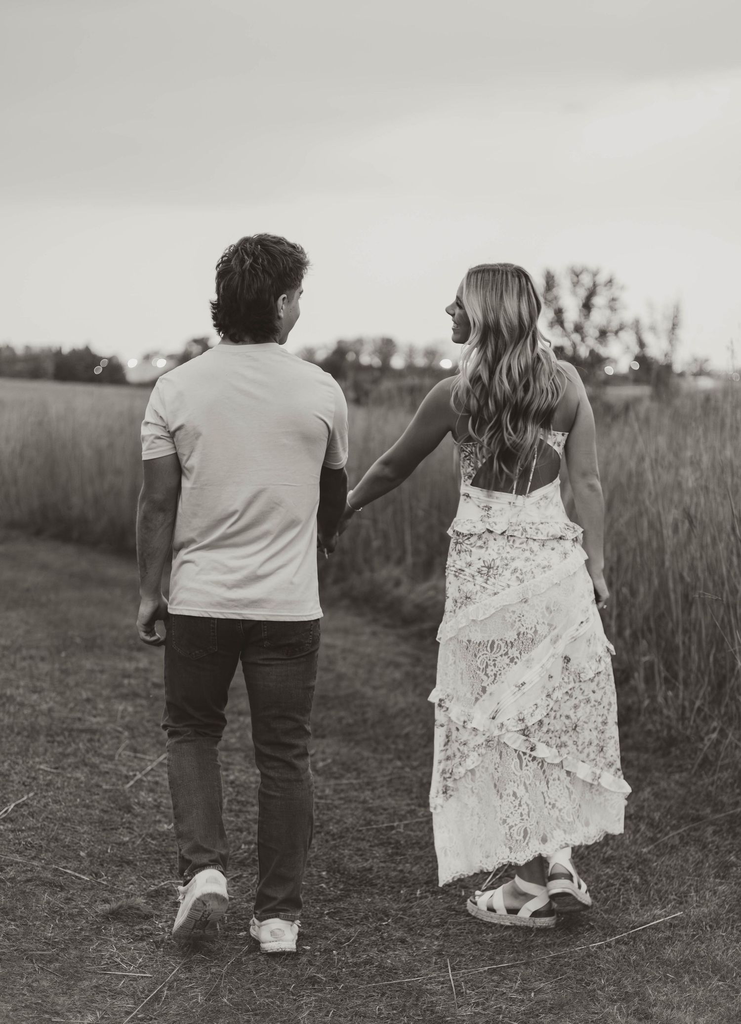 A couple walks hand in hand through a meadow in black and white photography.