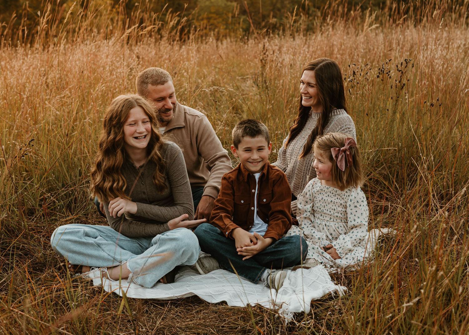 Family enjoys a cozy autumn picnic together on a blanket surrounded by golden tall grass at sunset.