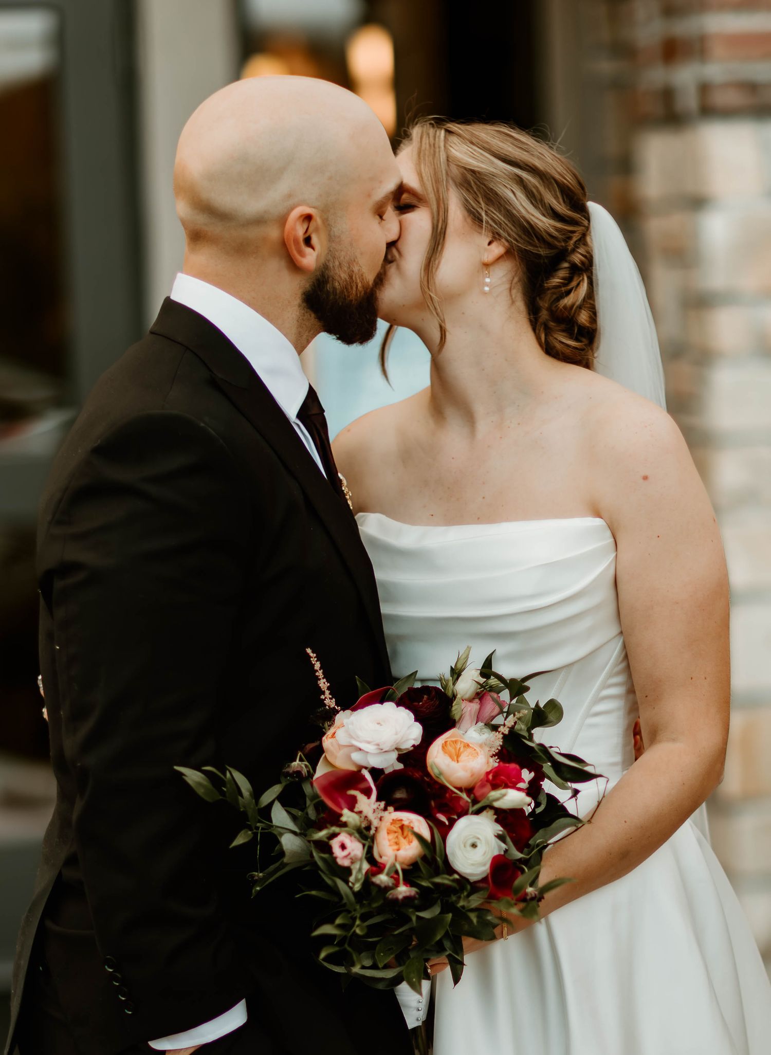 Wedding couple with elegant bouquet featuring deep red and pink flowers.