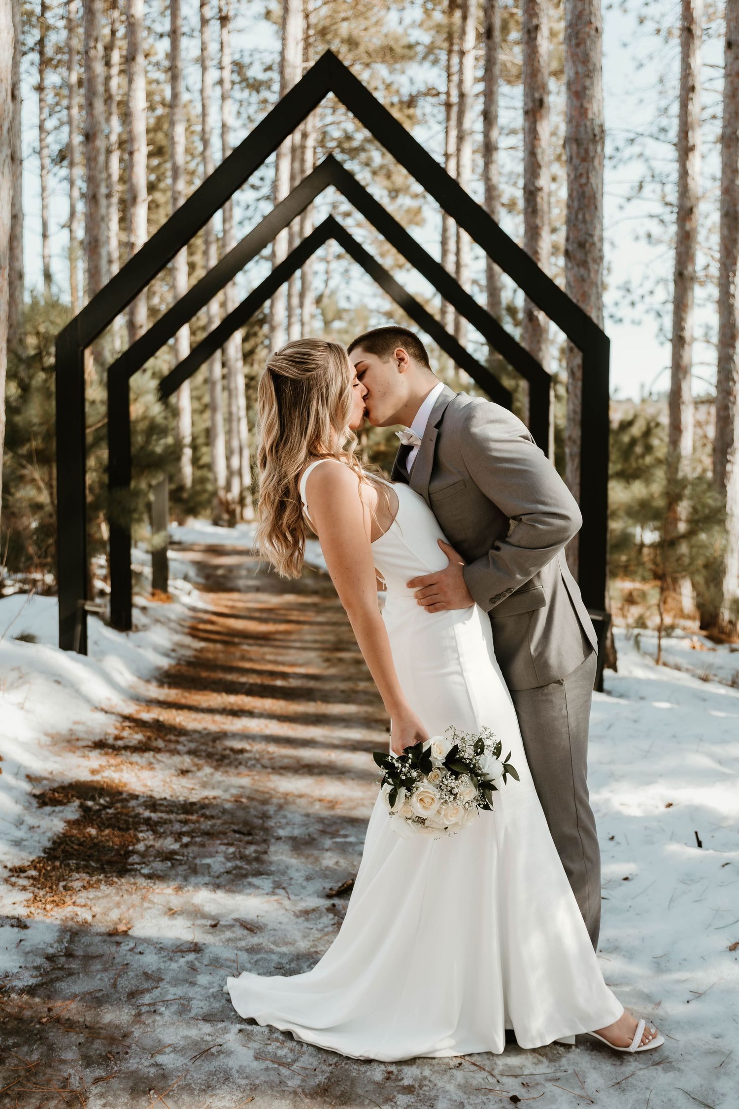 Winter wedding photography with geometric black arches in snowy pine forest.