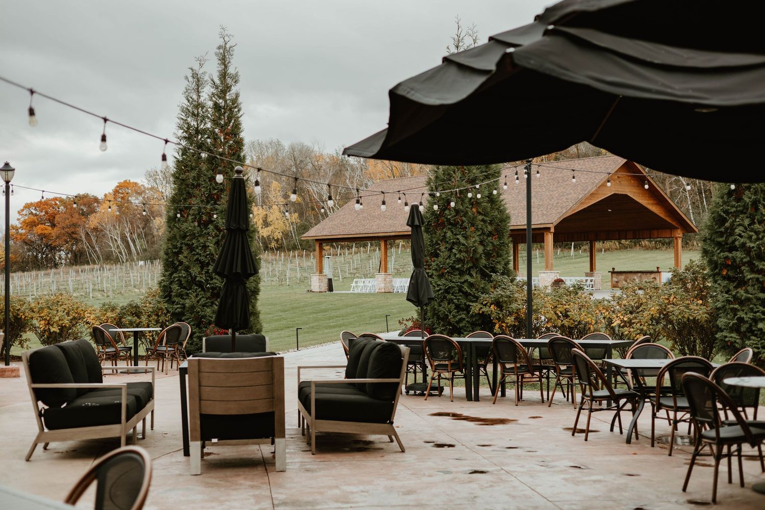 A rustic outdoor patio area with string lights and wooden furniture arranged for dining and lounging.