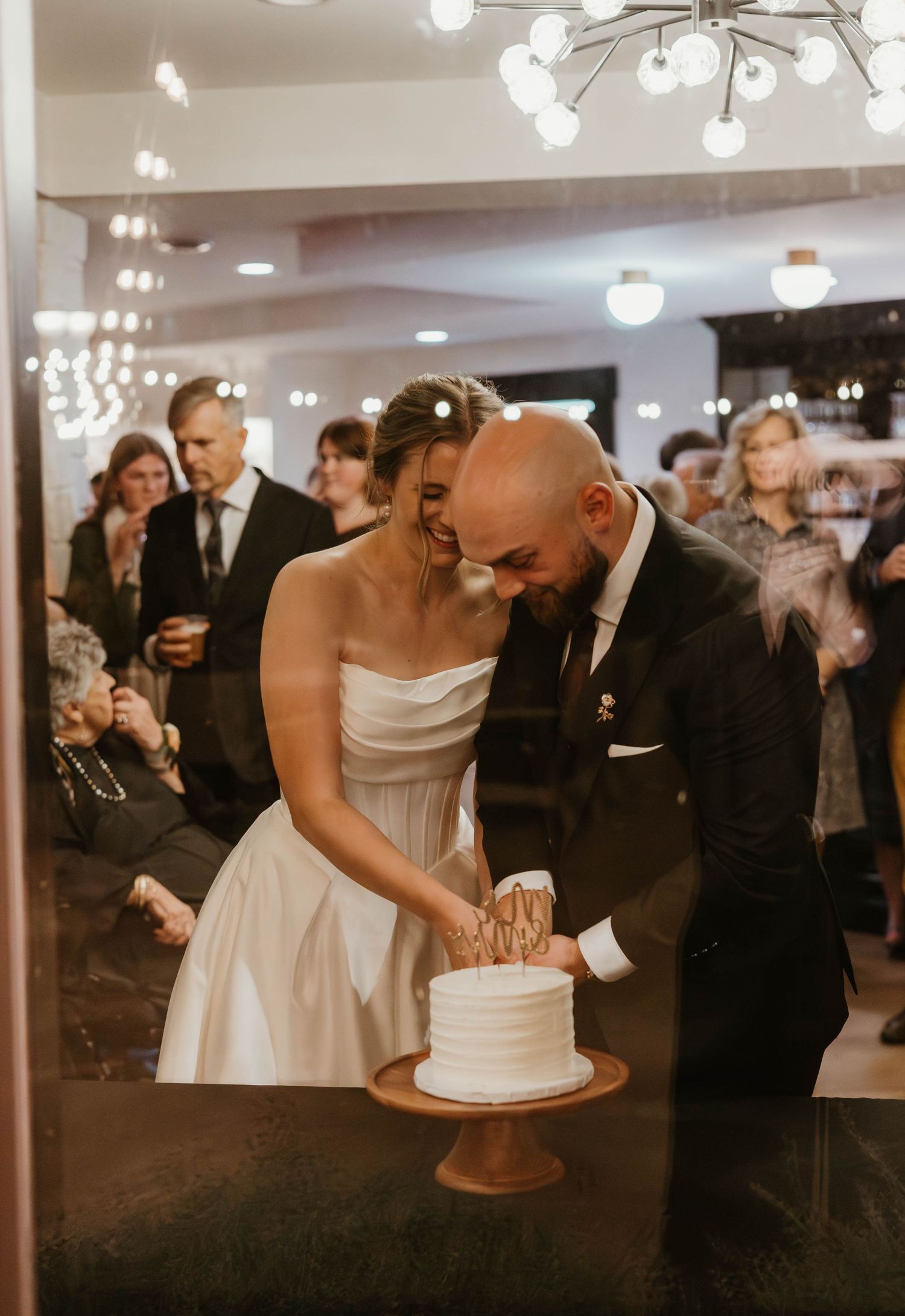 Wedding reception cake cutting moment with guests watching and taking photos.