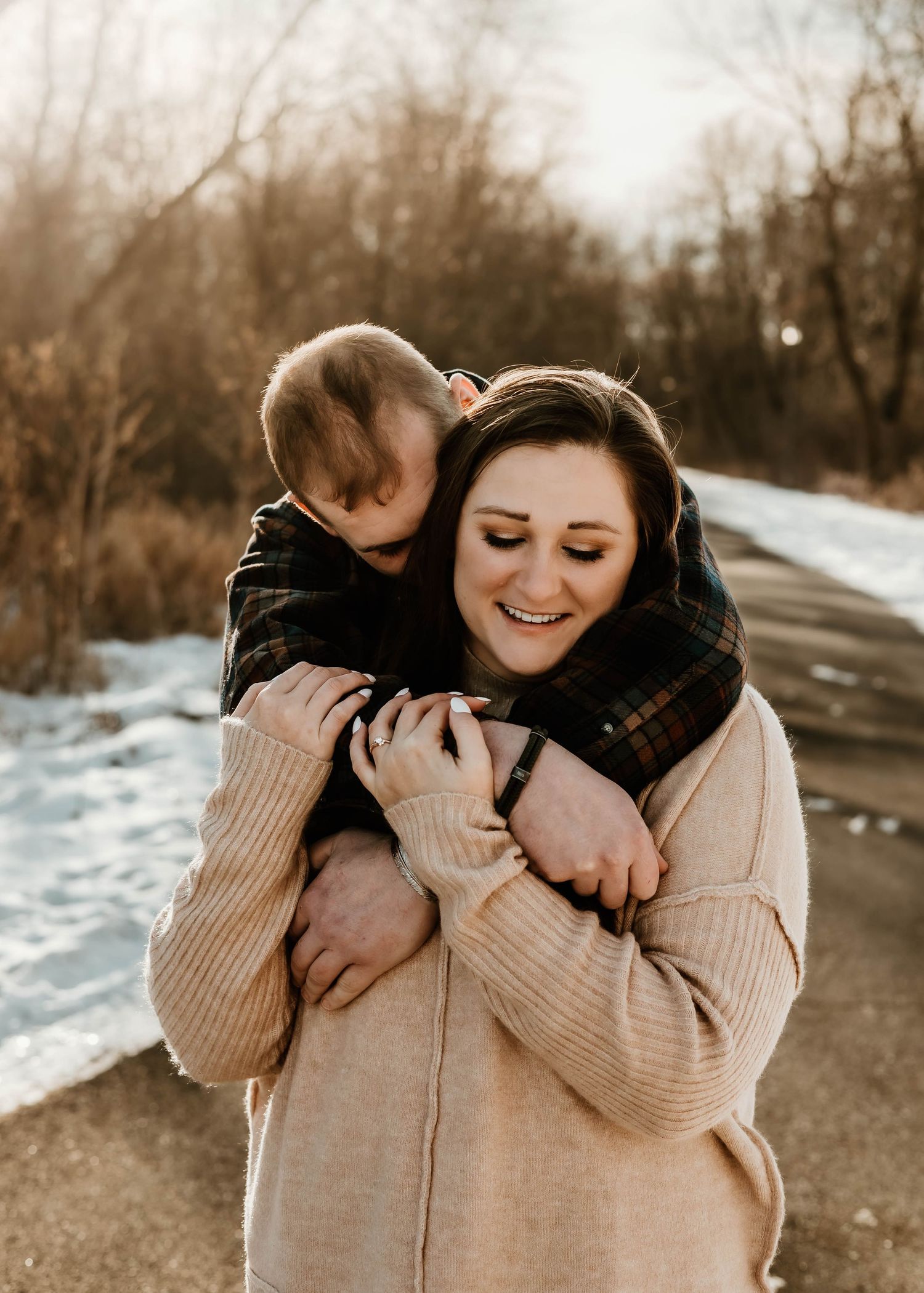 A parent and child share a joyful embrace on a snowy winter path while wearing cozy sweaters.