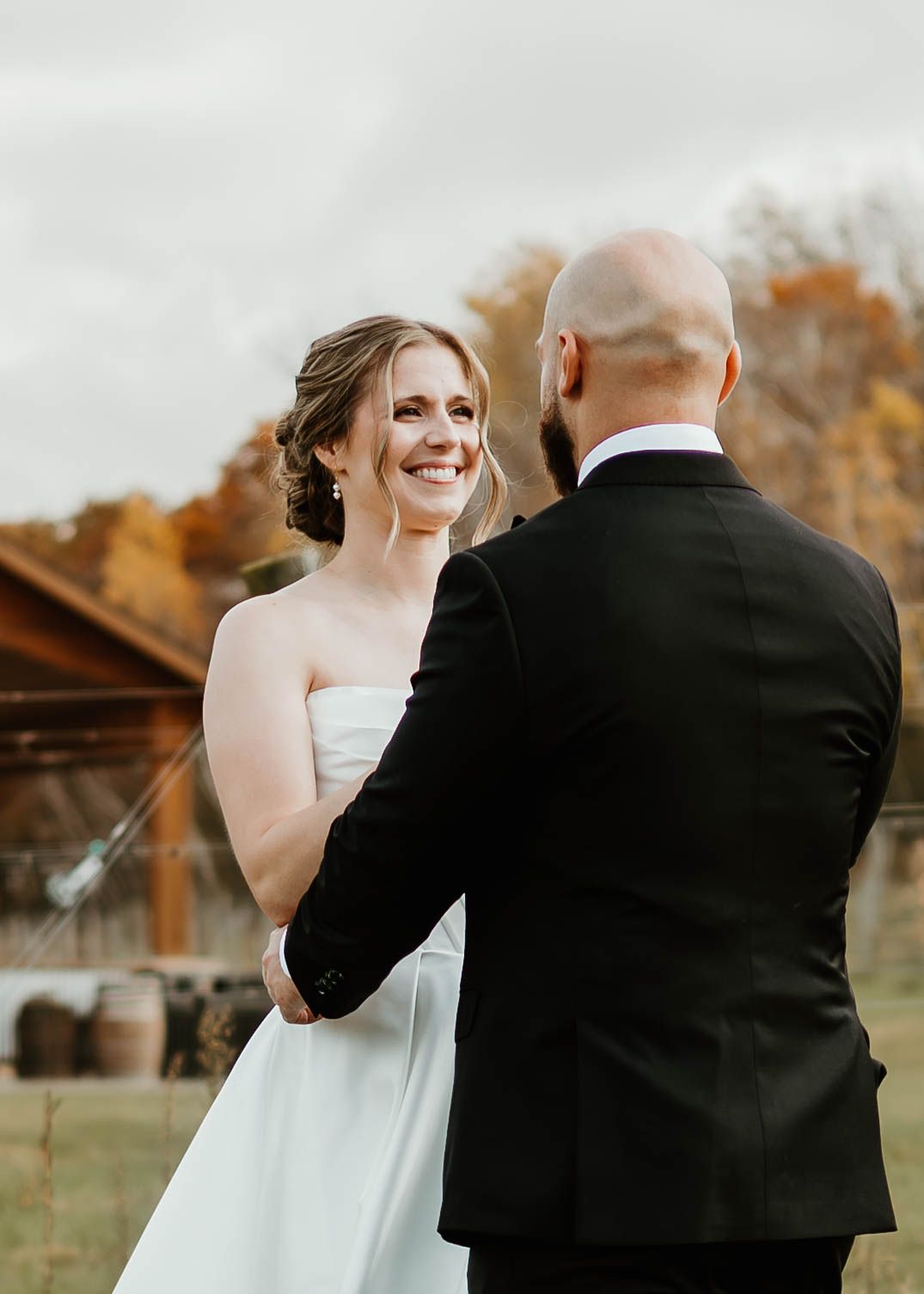 A couple shares a romantic moment outdoors during an autumn wedding photoshoot in a rustic setting.
