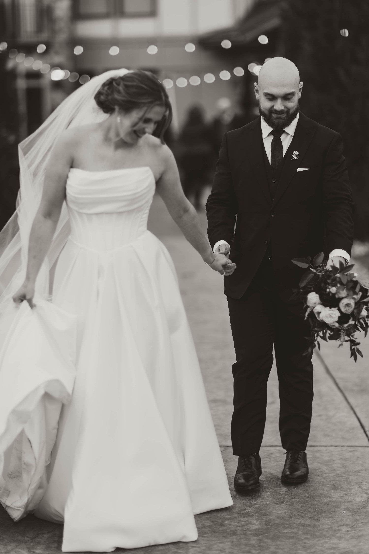 Black and white photos showing the flowing movement of a bride's dress with string lights overhead.