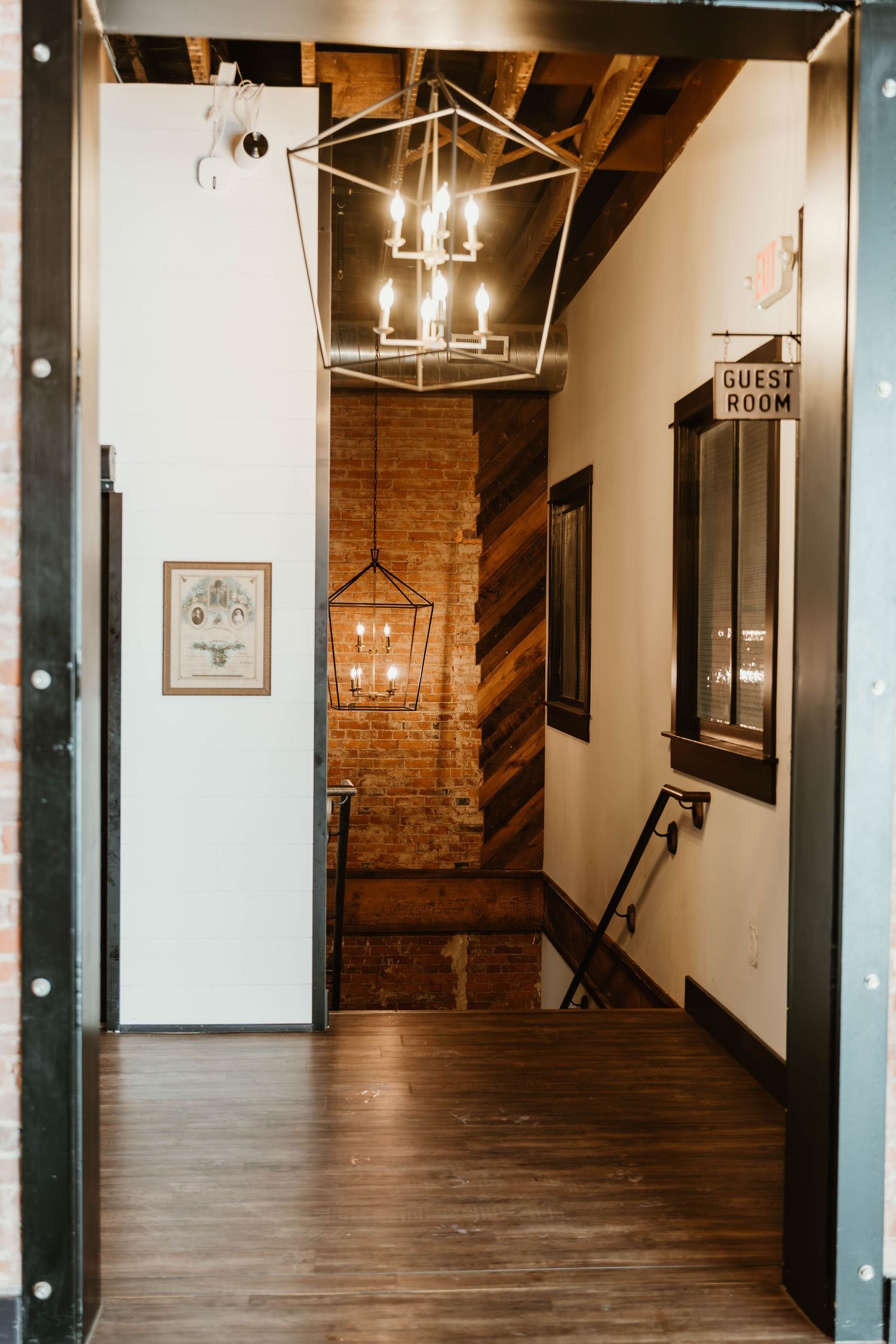 Industrial chic hallway with exposed brick walls, hardwood floors, and modern lantern pendant lights.