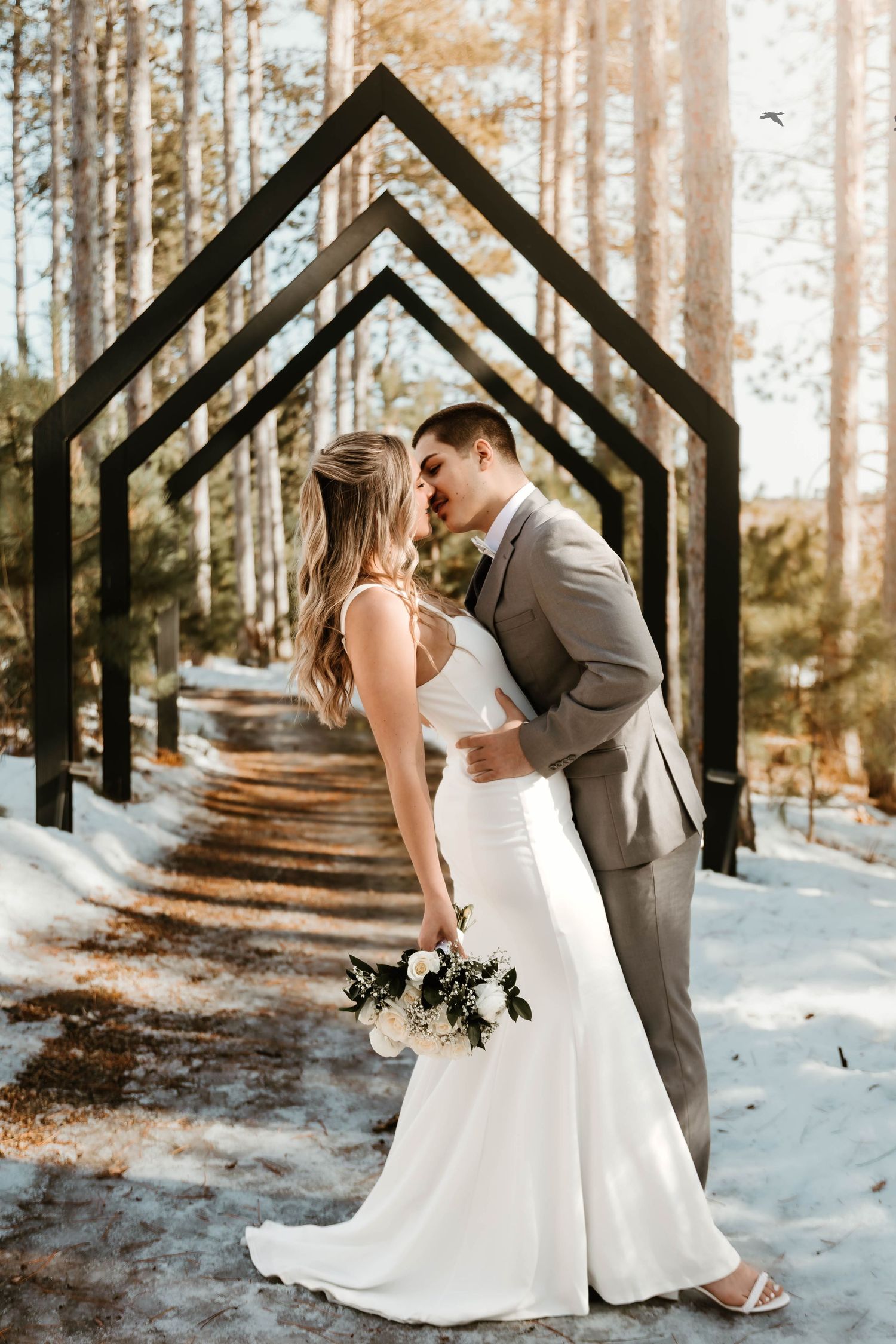 Winter wedding photoshoot in a snow-covered forest with geometric black arches framing the scene.