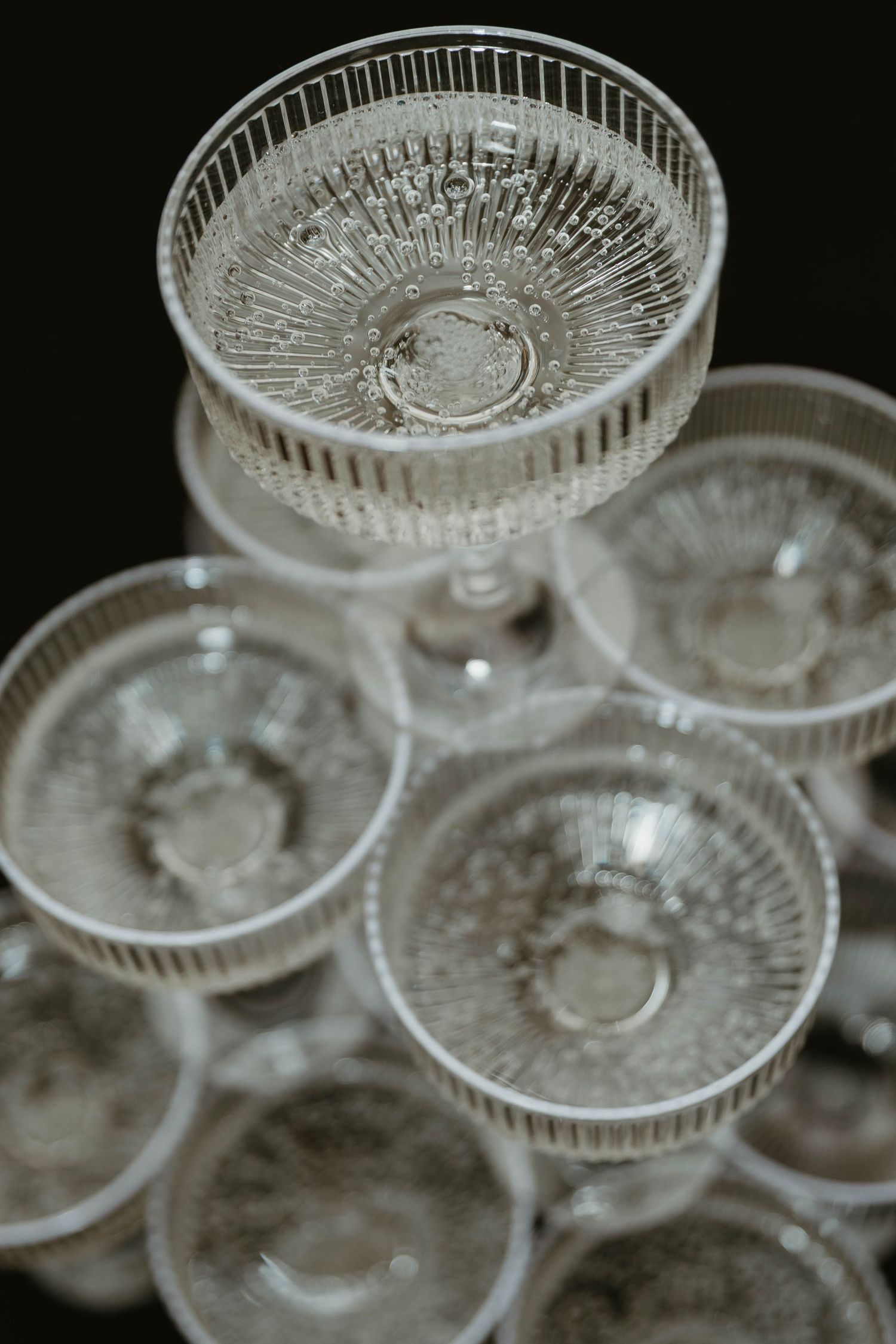 Crystal champagne coupes arranged in a geometric pattern against a dark background.