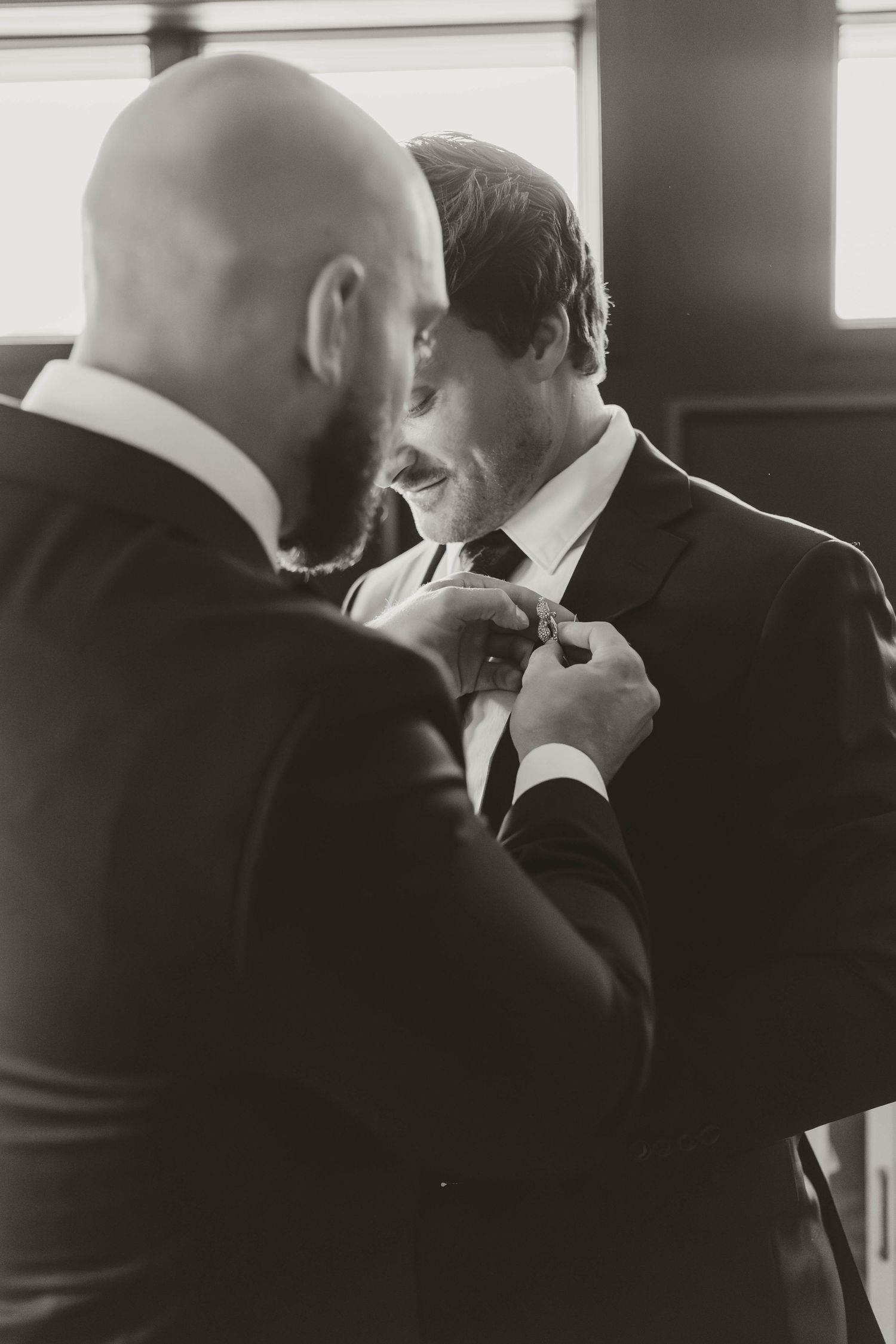 A tender moment between two people in formal attire adjusting a tie before the ceremony.