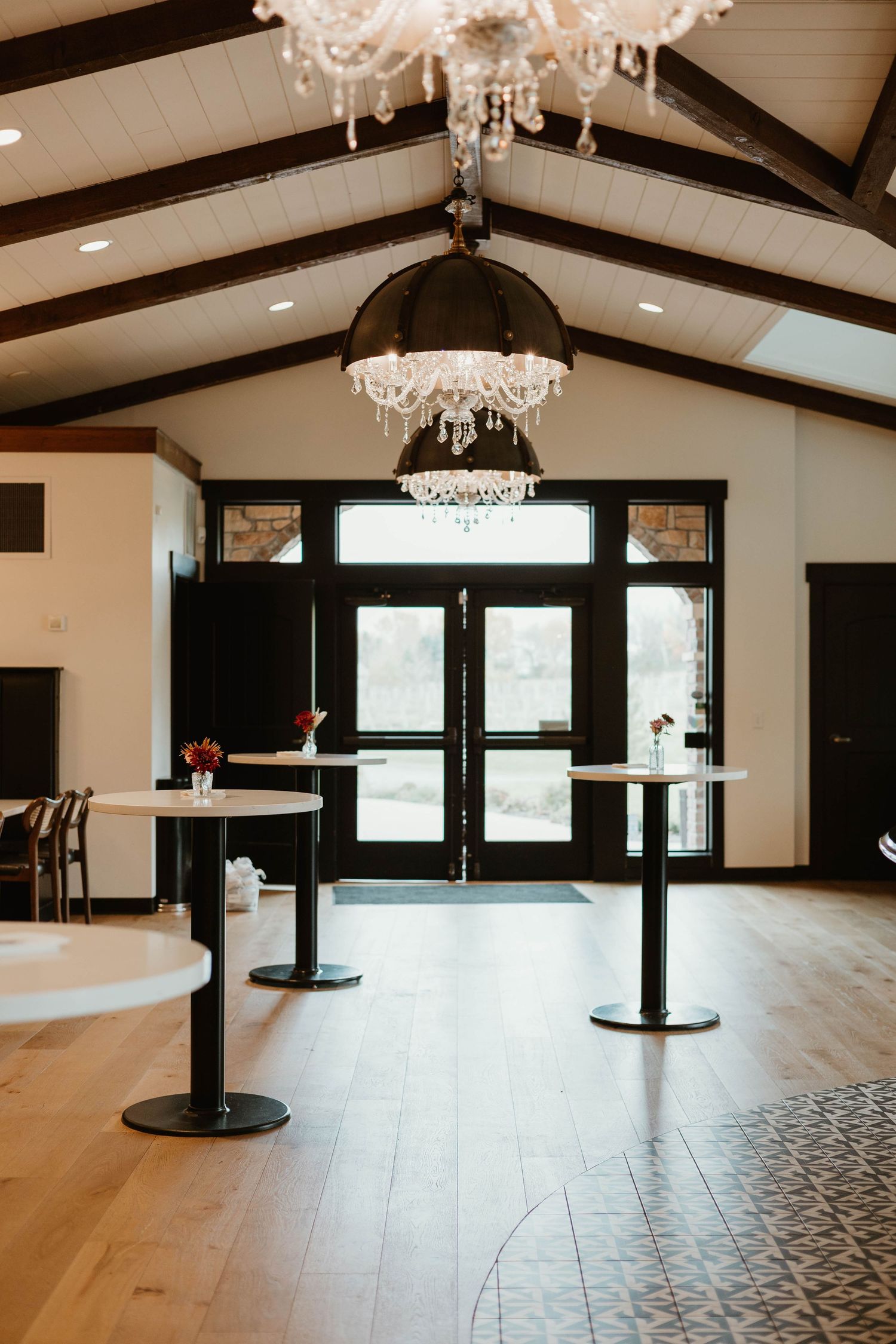 An elegant event venue interior with crystal chandeliers, exposed beams, and hardwood floors.
