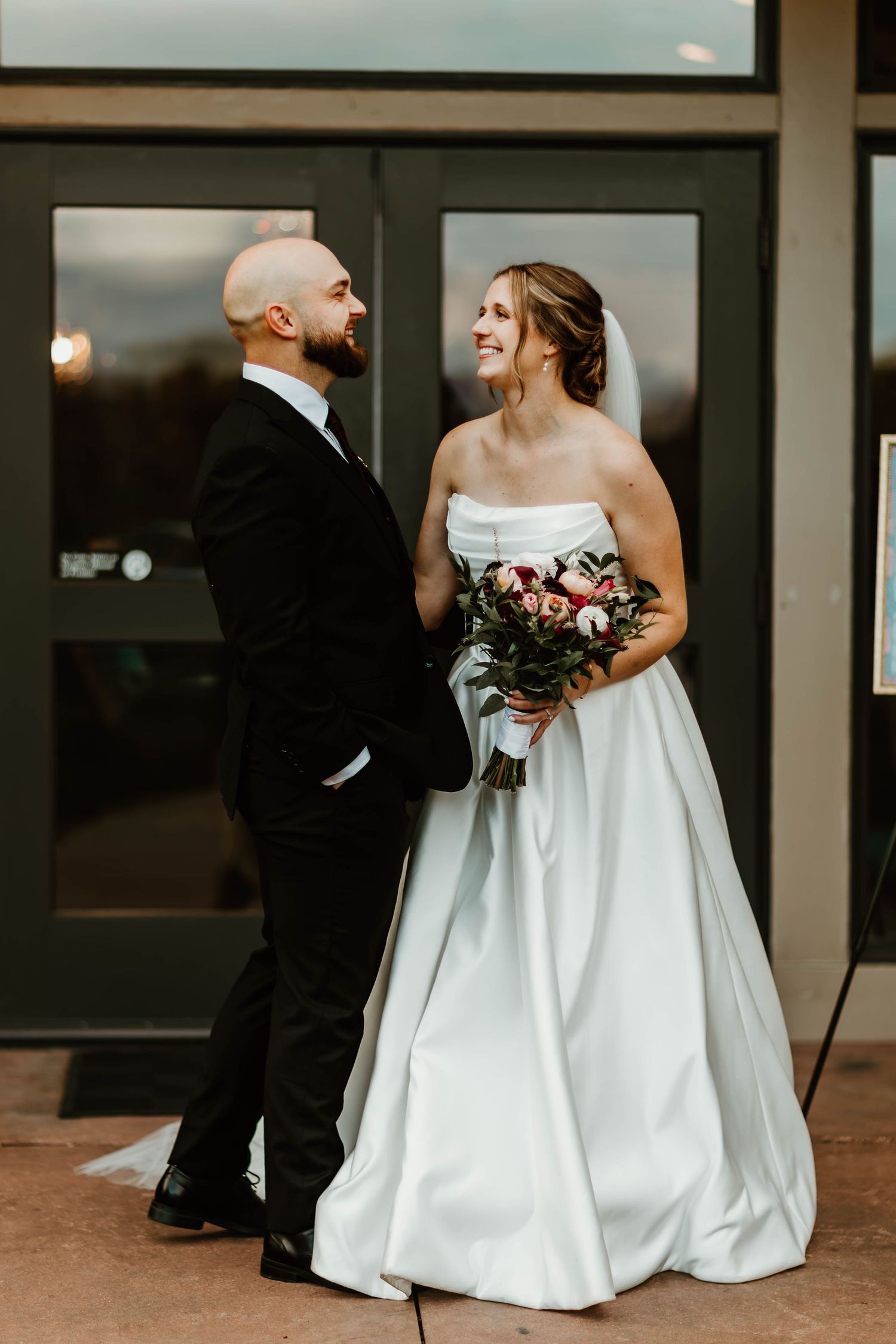 Wedding couple in formal attire sharing a candid moment on a patio.