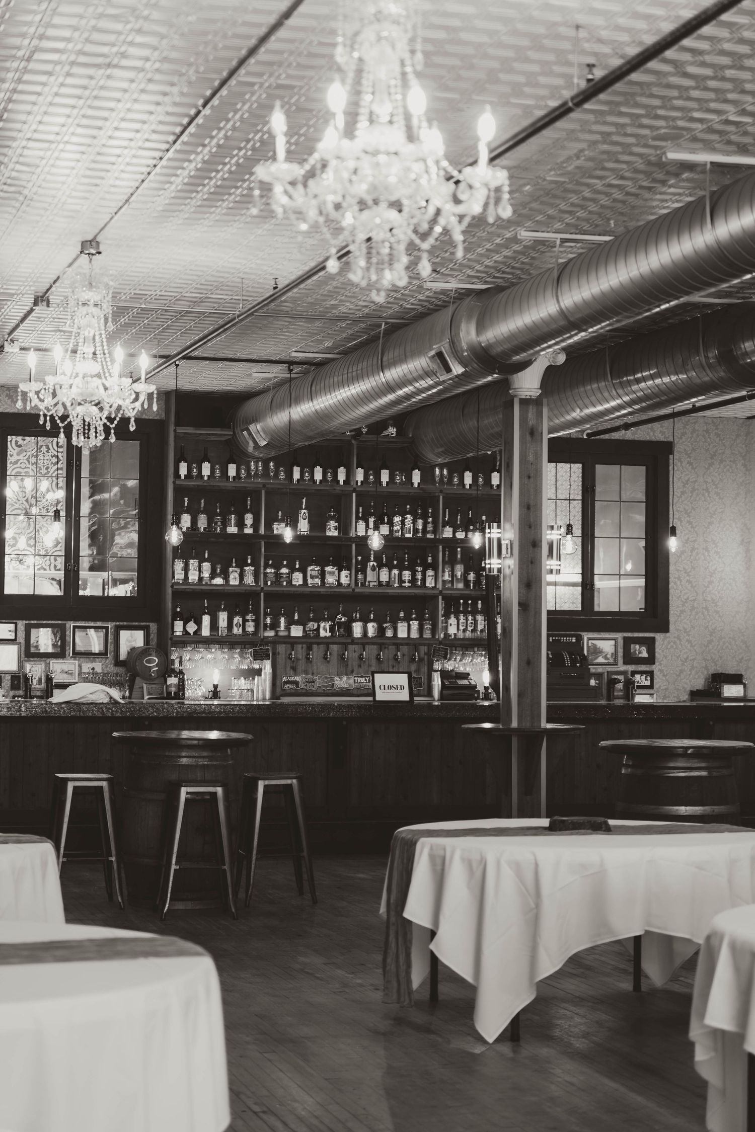 Elegant bar interior with crystal chandeliers, white tablecloths, and fully stocked shelves in a dimly lit space.
