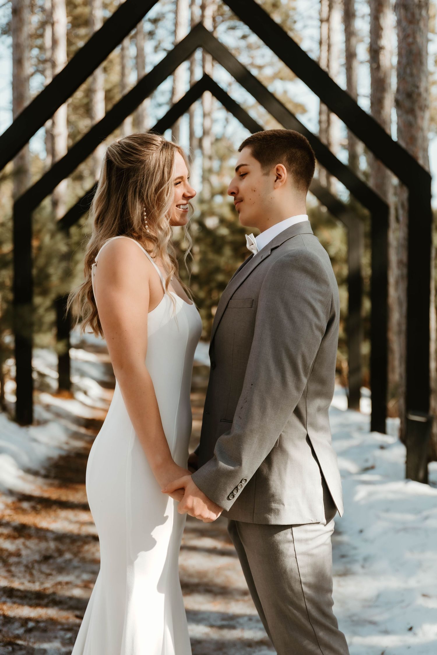 Winter wedding scene with snow covered trees and geometric wooden archway.