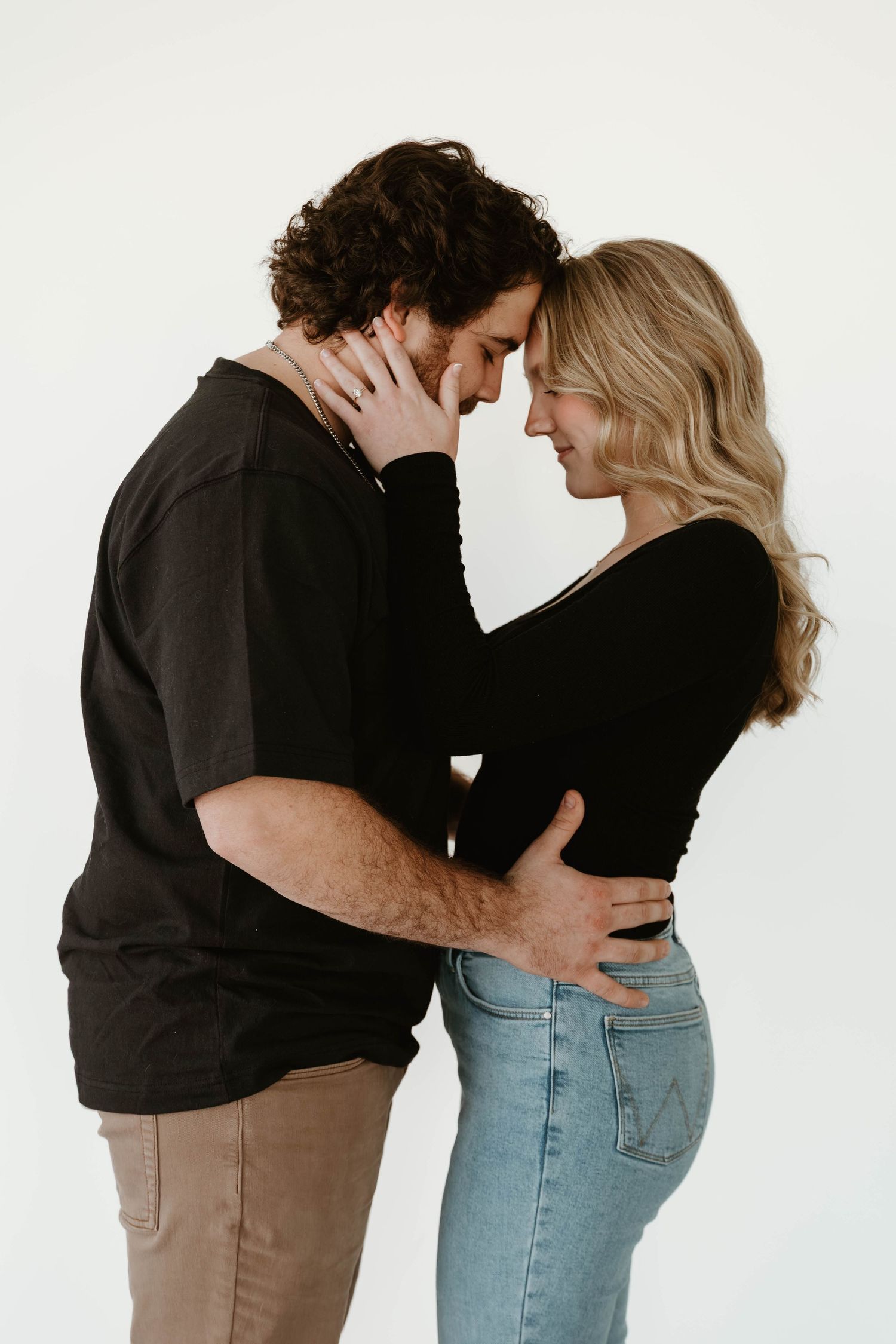 A romantic couple embraces while wearing matching black tops against a minimalist white backdrop.