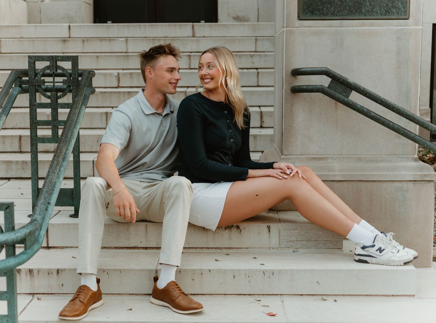 A couple sits casually on white steps while wearing casual clothing and sneakers.