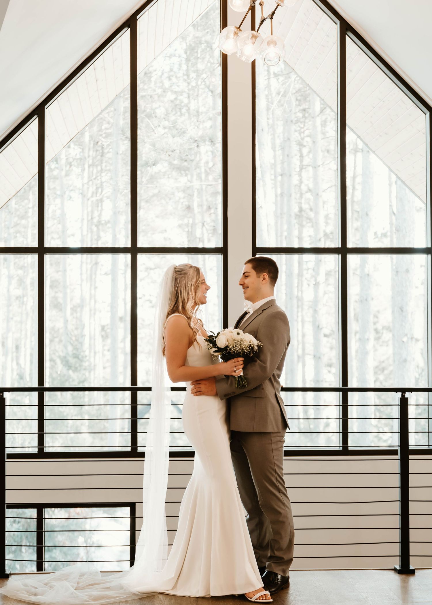 Wedding ceremony in modern chapel with floor-to-ceiling windows overlooking snowy forest.
