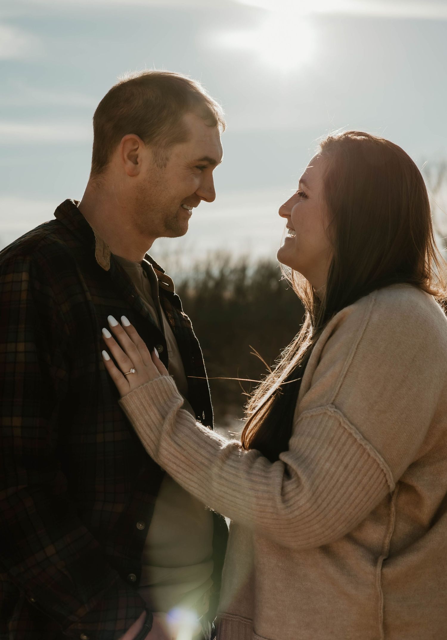 A couple embraces in warm sunlight against a backlit sky during a romantic outdoor photo session.