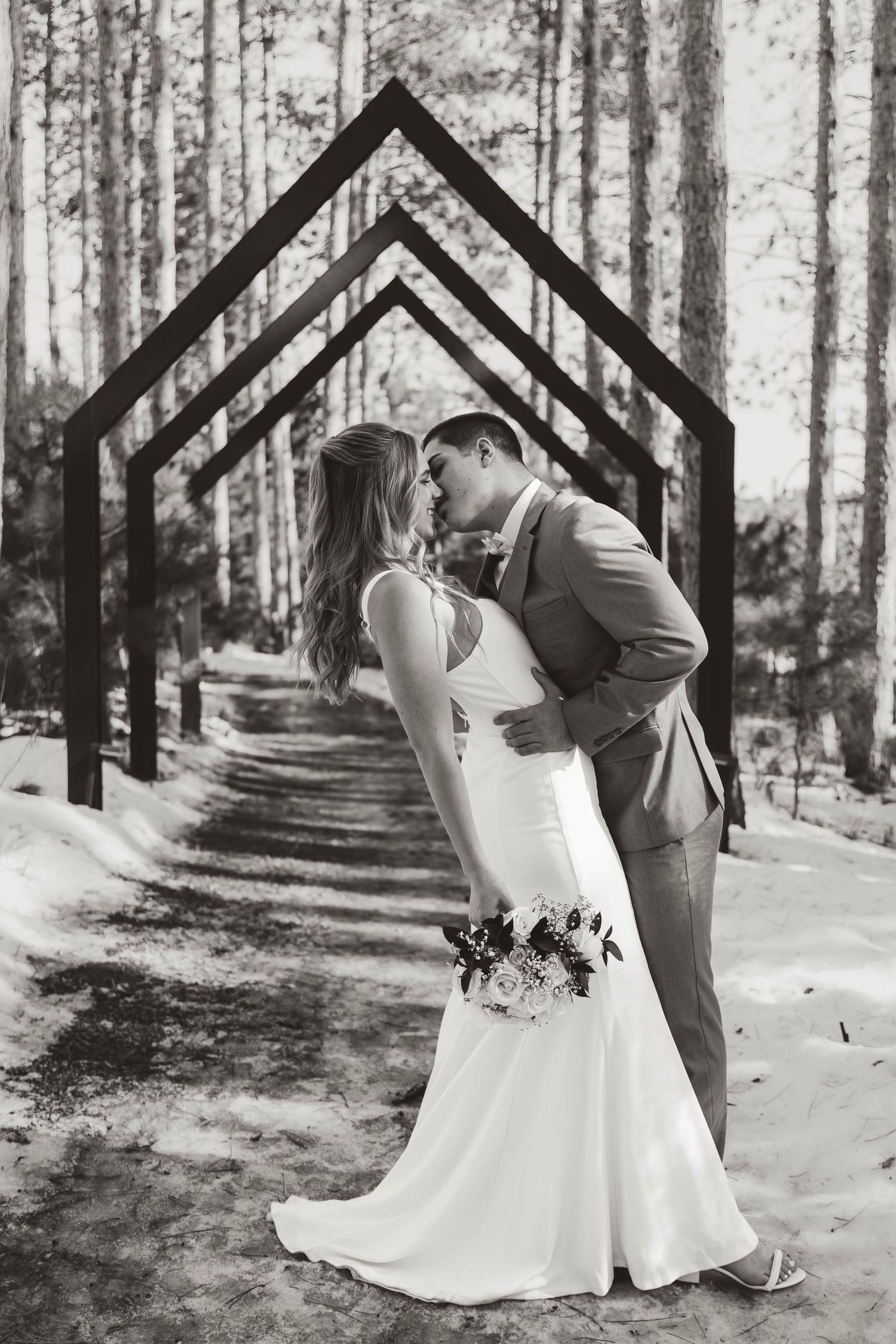Wedding couple poses among tall pine trees in a romantic black and white photo series.