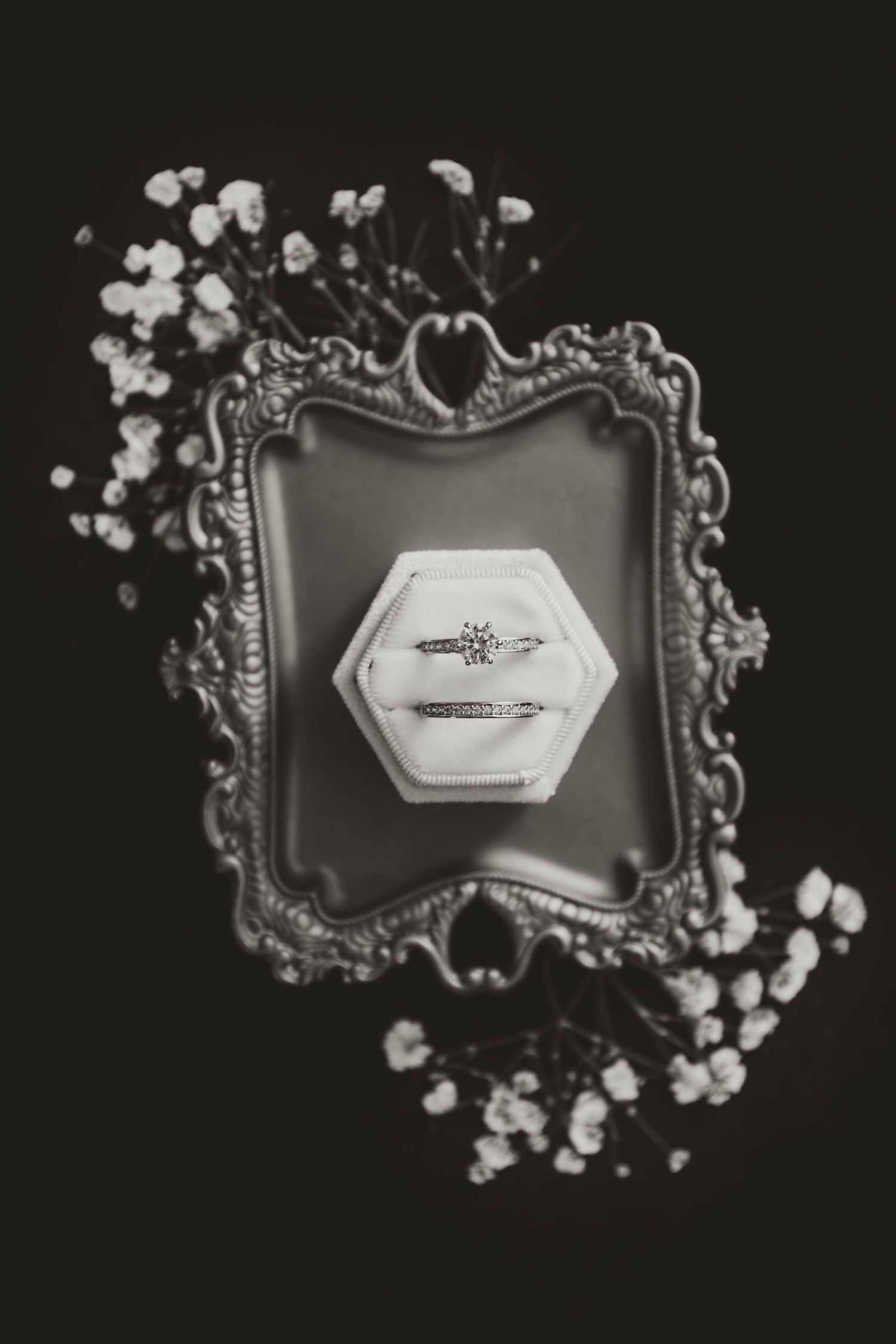 Wedding rings in hexagonal ring box displayed on antique silver tray with baby's breath flowers.
