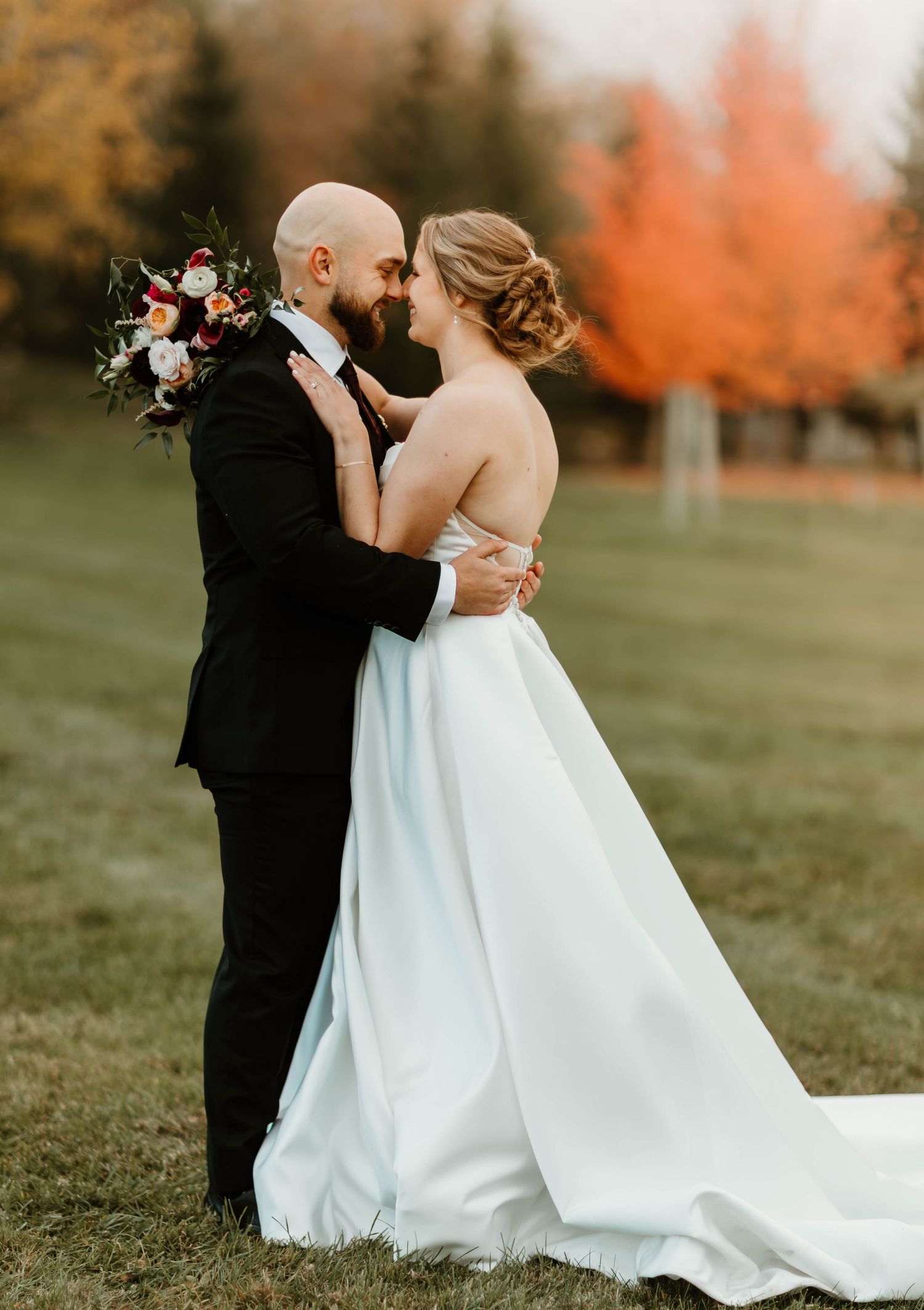 Autumn wedding photography with couple embracing in a field with orange foliage.