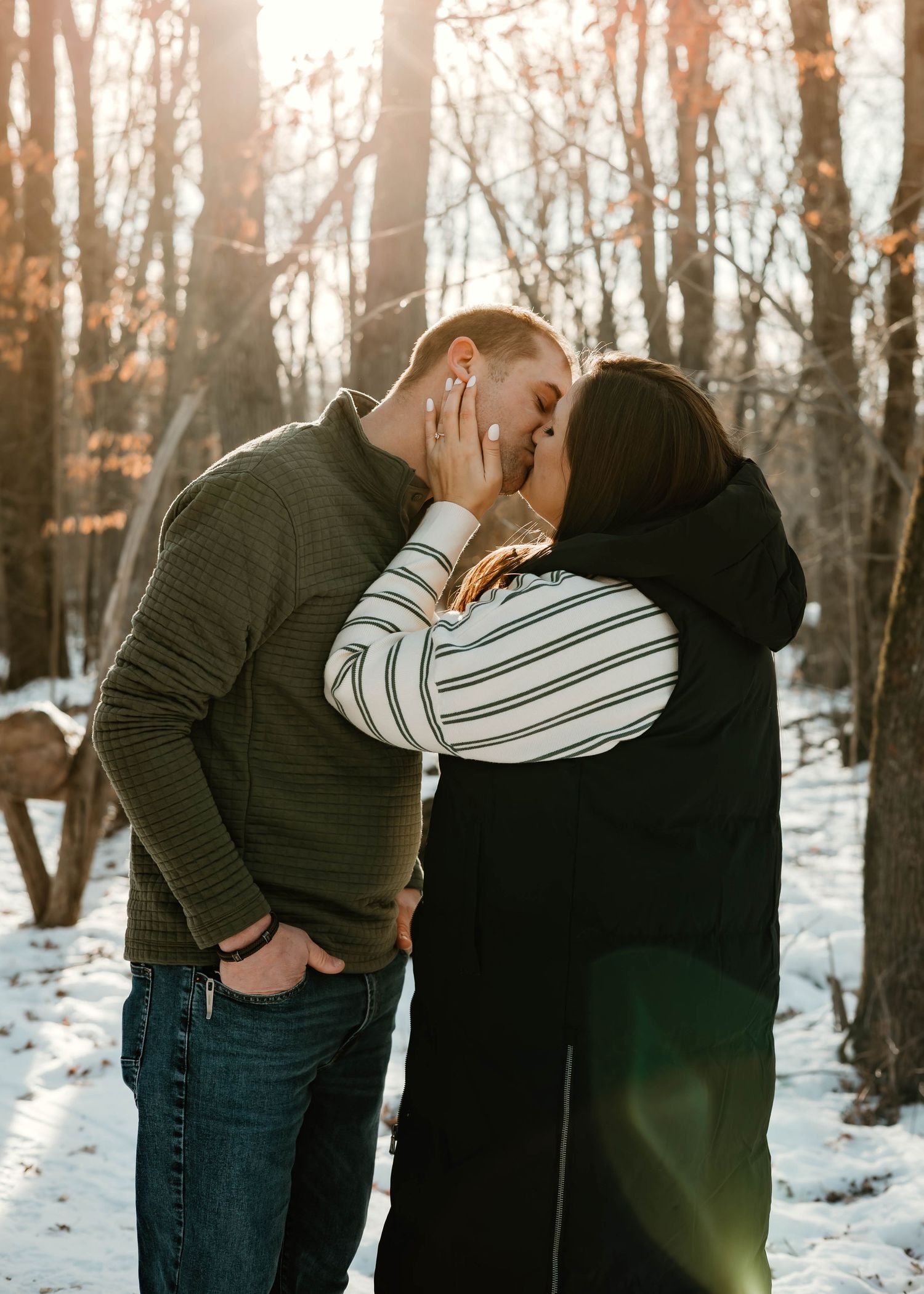 A couple embraces in a romantic dance pose surrounded by snow-covered trees at sunset.