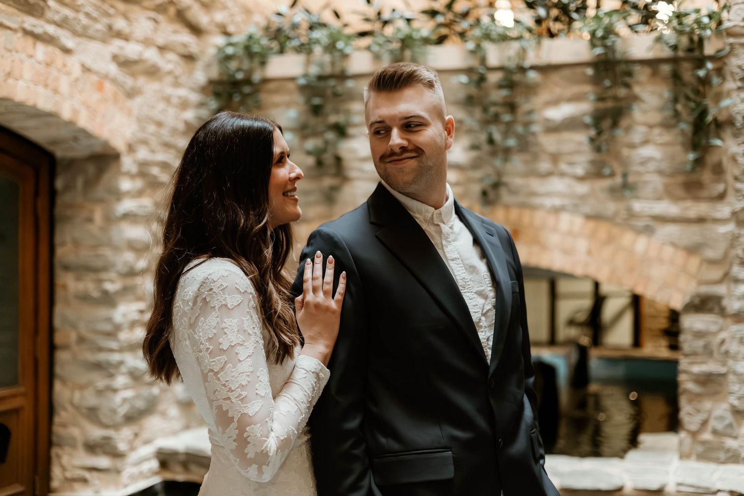 A couple embraces on a rustic stone patio with natural lighting and architectural details in the background.