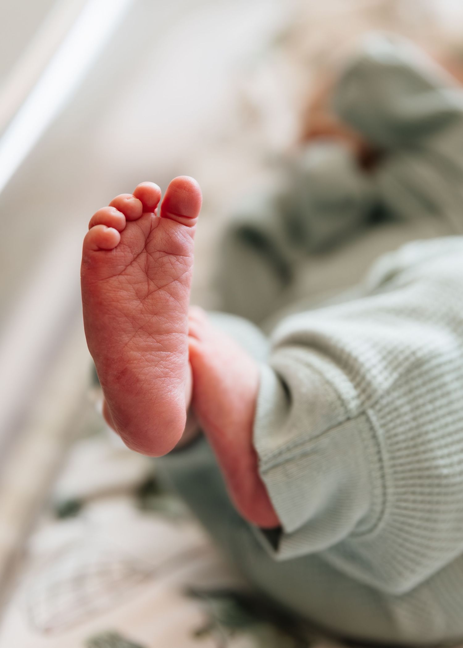 Close-up of a newborn baby's tiny foot wearing a soft green onesie, captured in natural light.