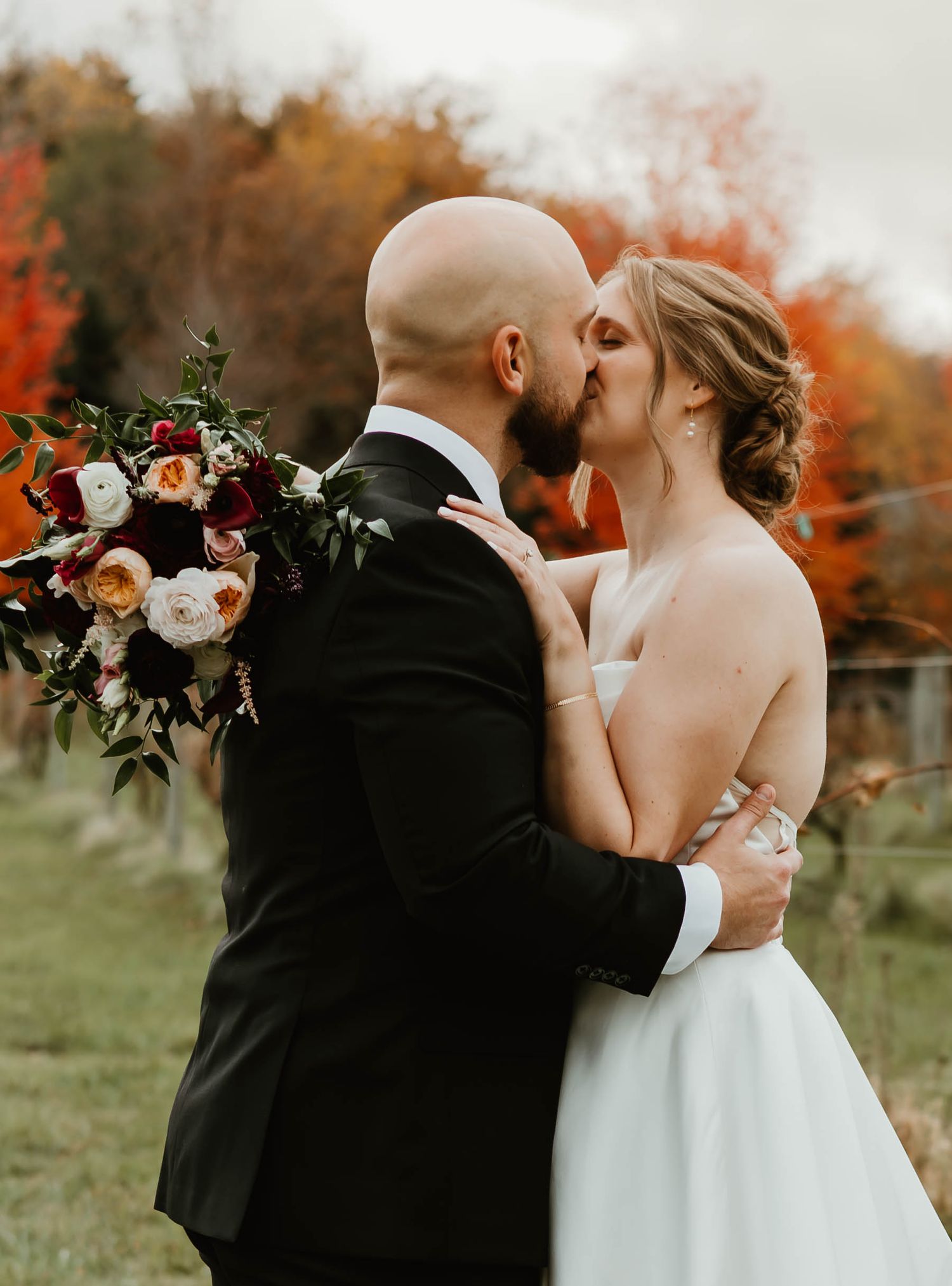 Wedding couple sharing intimate moment in autumn field with floral bouquet.