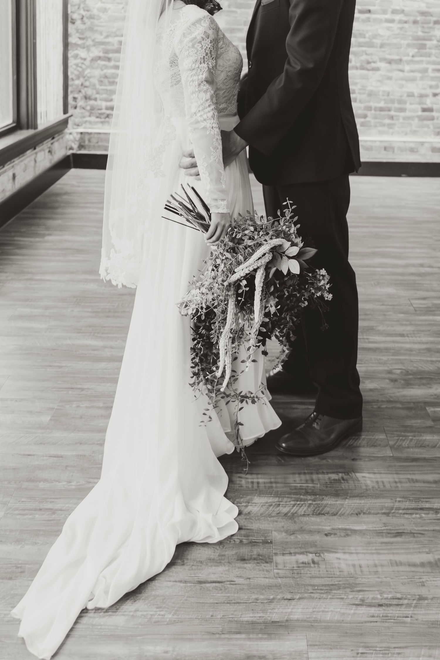 Black and white wedding photo showing dress details and floral bouquet.