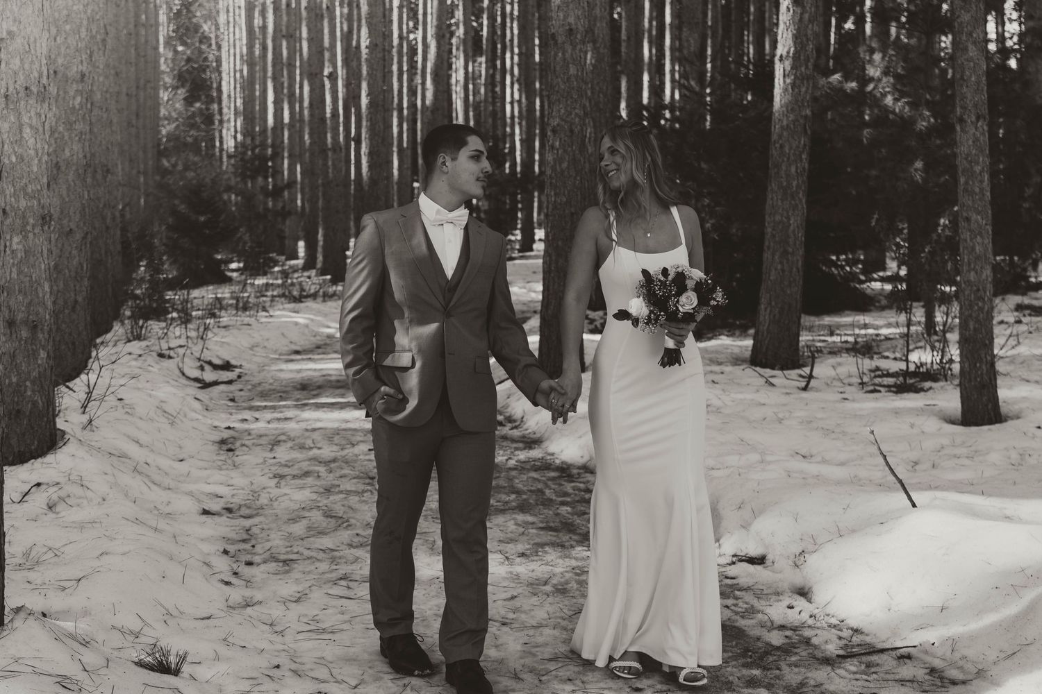 Black and white wedding photography in a serene forest setting with snow-covered ground.