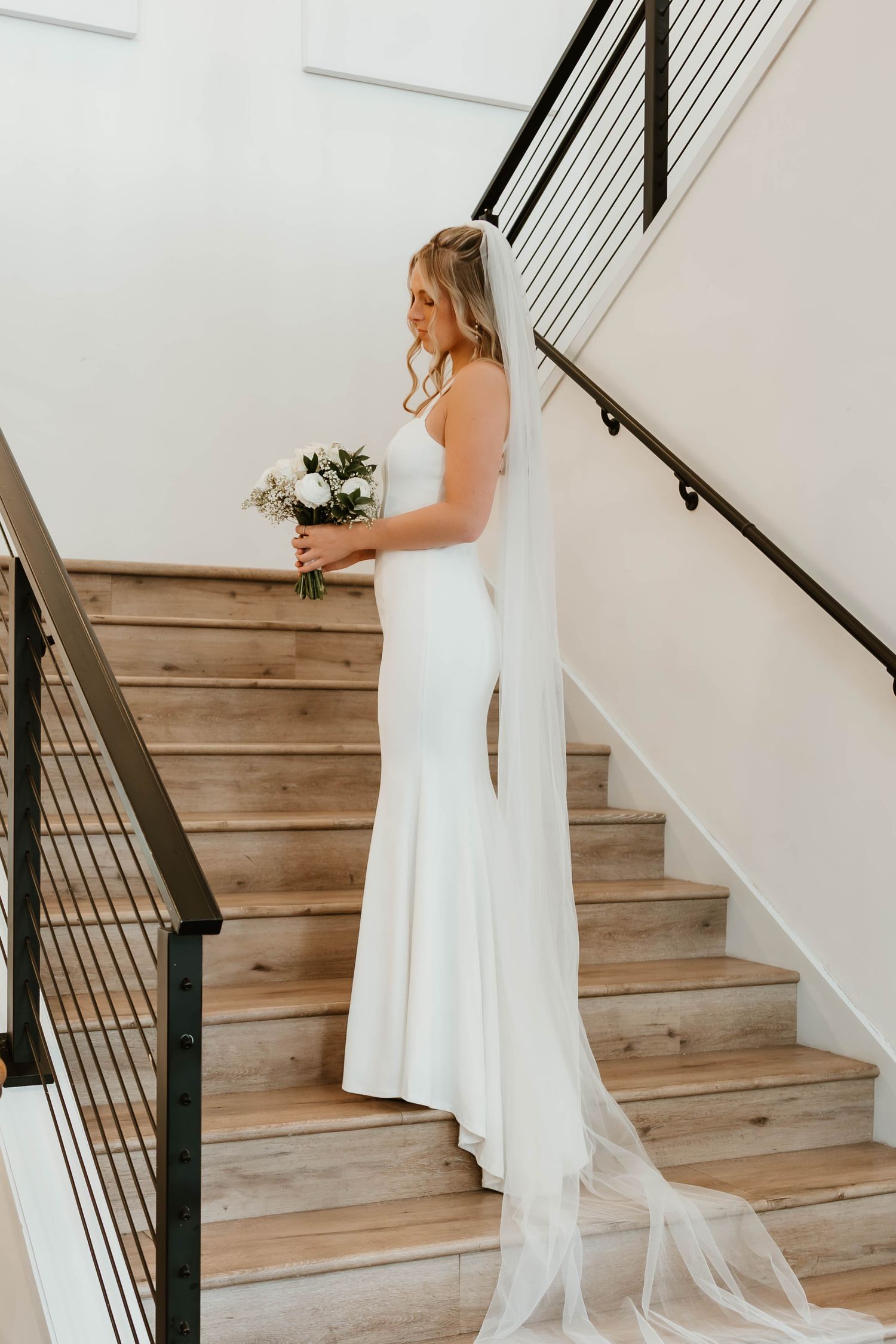 White wedding dress flowing down wooden staircase with modern black railing.