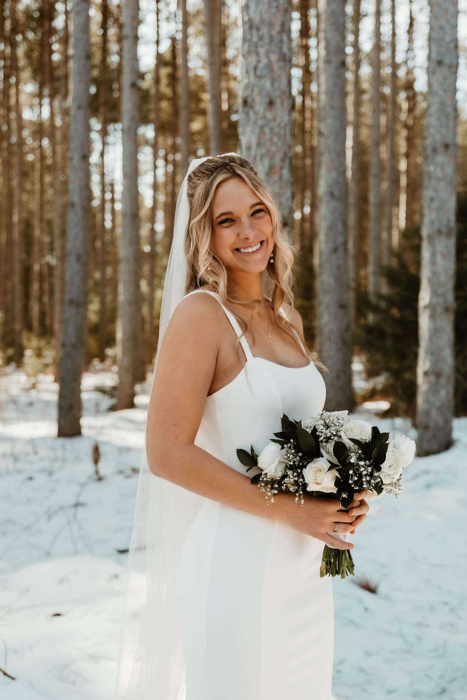 A winter bridal portrait session among snow-covered pine trees featuring a white bouquet.