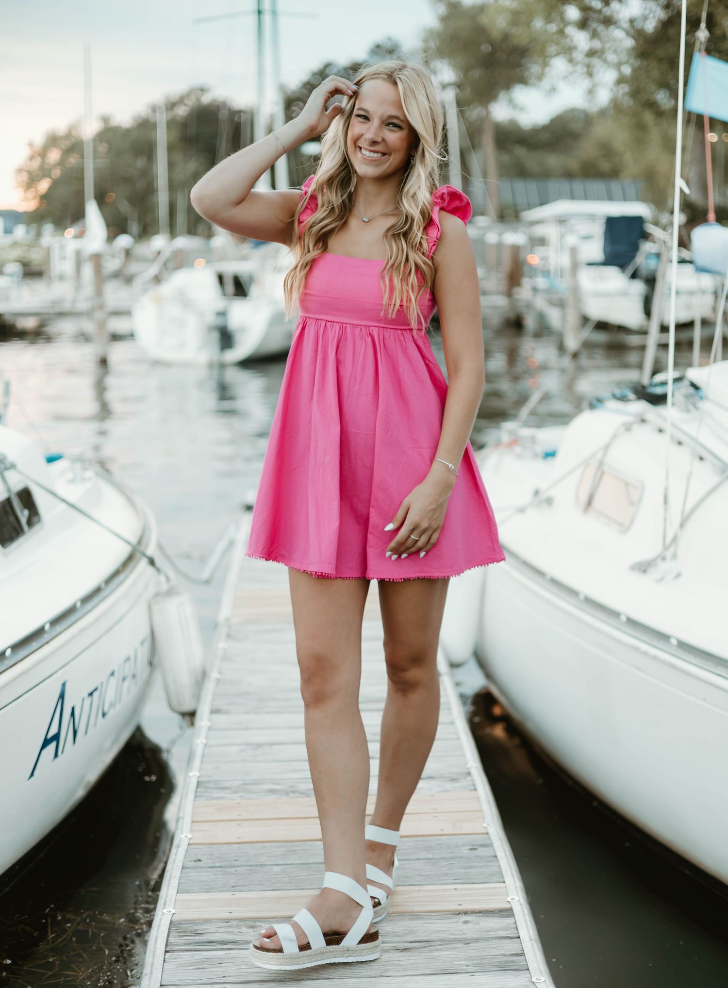 A series of photos showing someone in a pink dress and white sandals posing on a wooden dock near sailboats.