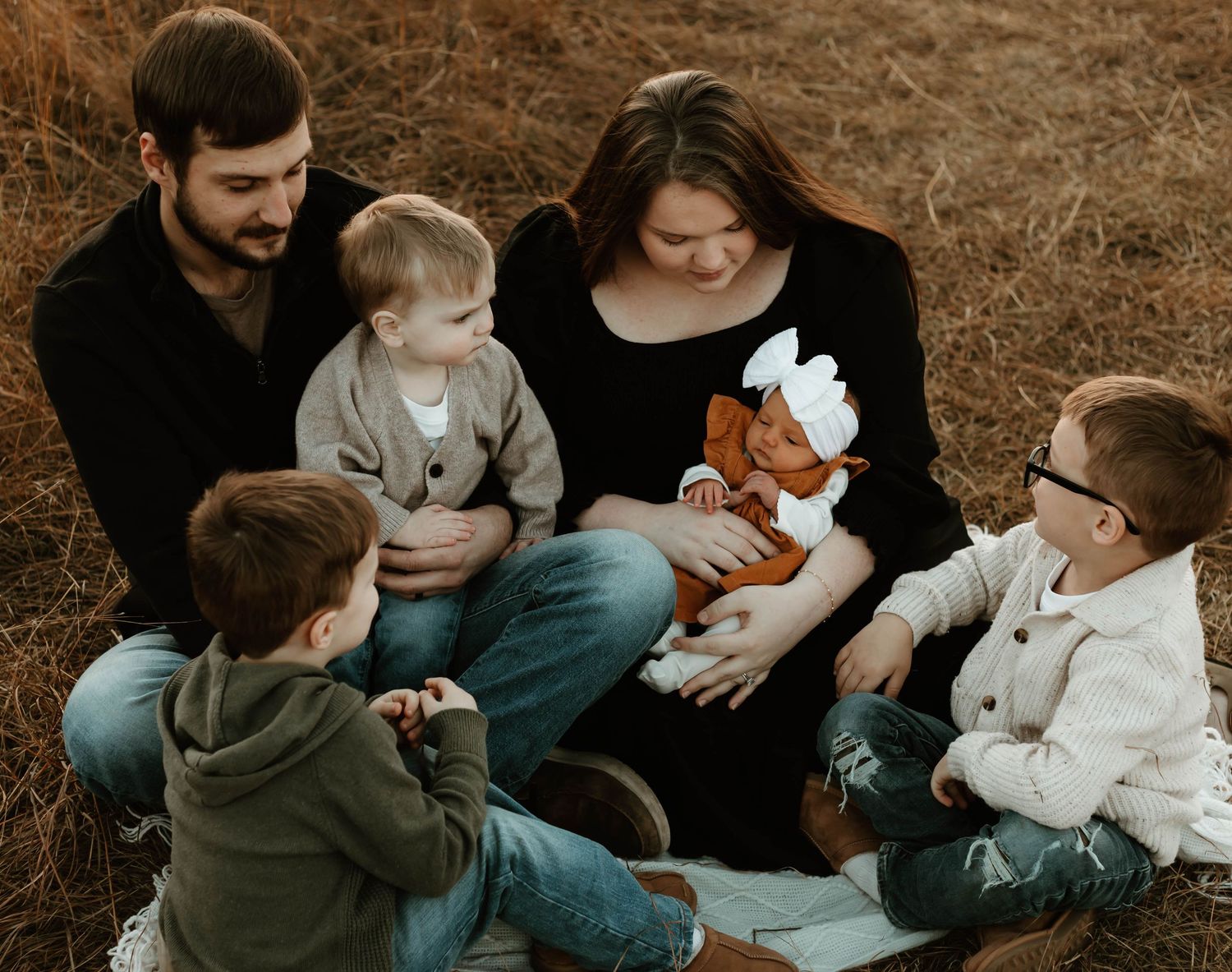 Family sitting together on brown grass during autumn with a plush toy duck in a cozy outdoor gathering.