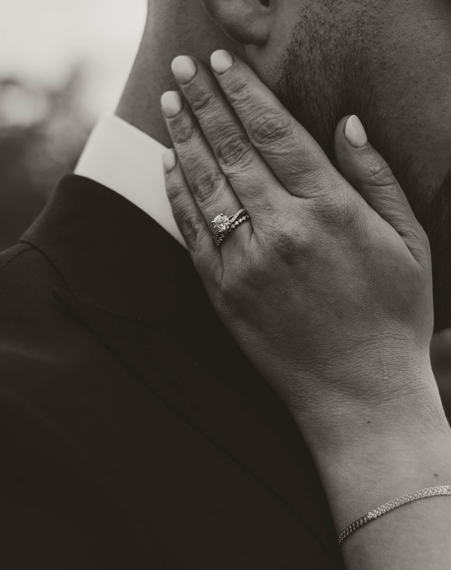 Close-up of a hand wearing wedding rings against formal attire.