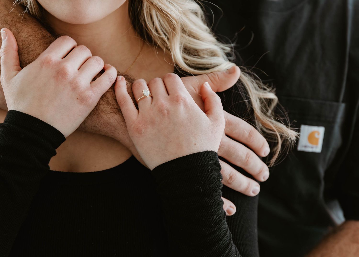 A person with long blonde hair wearing a black top holds their hands near their face in an expressive pose.