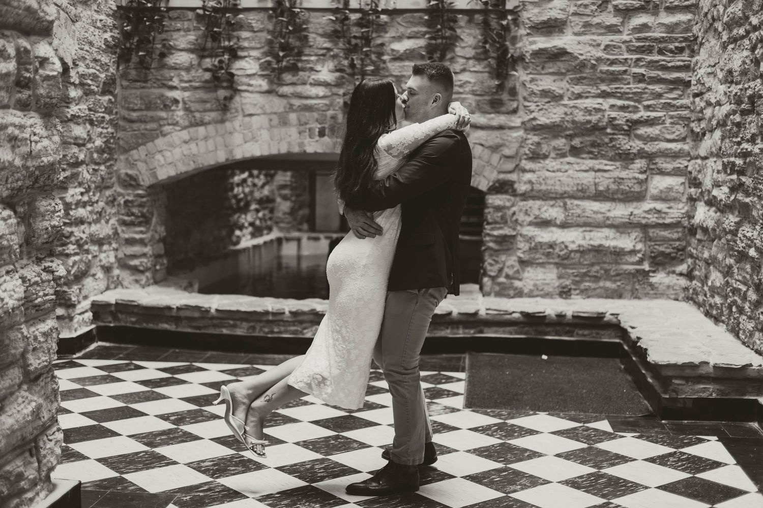 Wedding couple dancing on a vintage stone-walled room with black and white checkered flooring.
